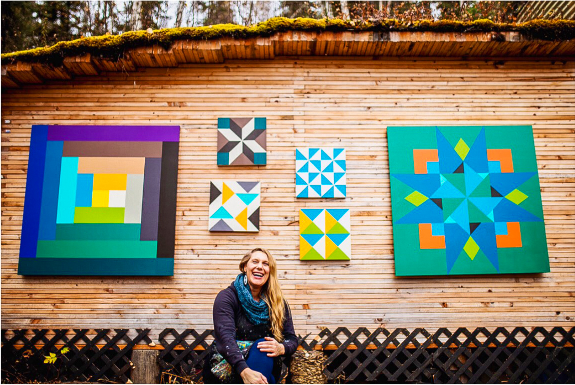 Woman seating down with a wall of quilts behind her
