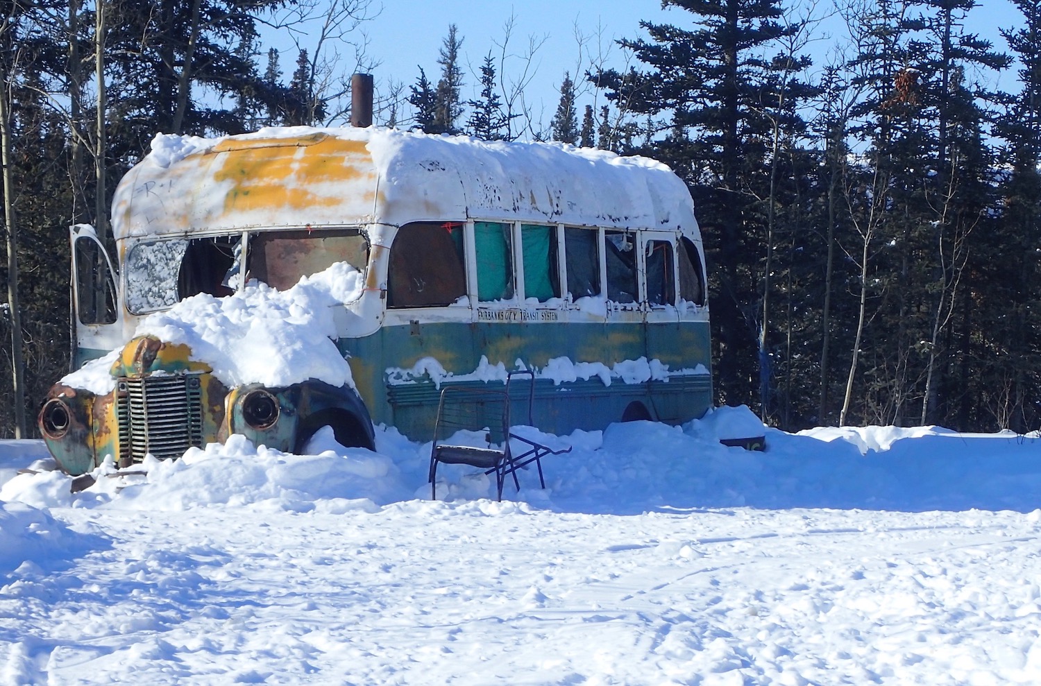 A bus covered in snow sits in a wooded area.