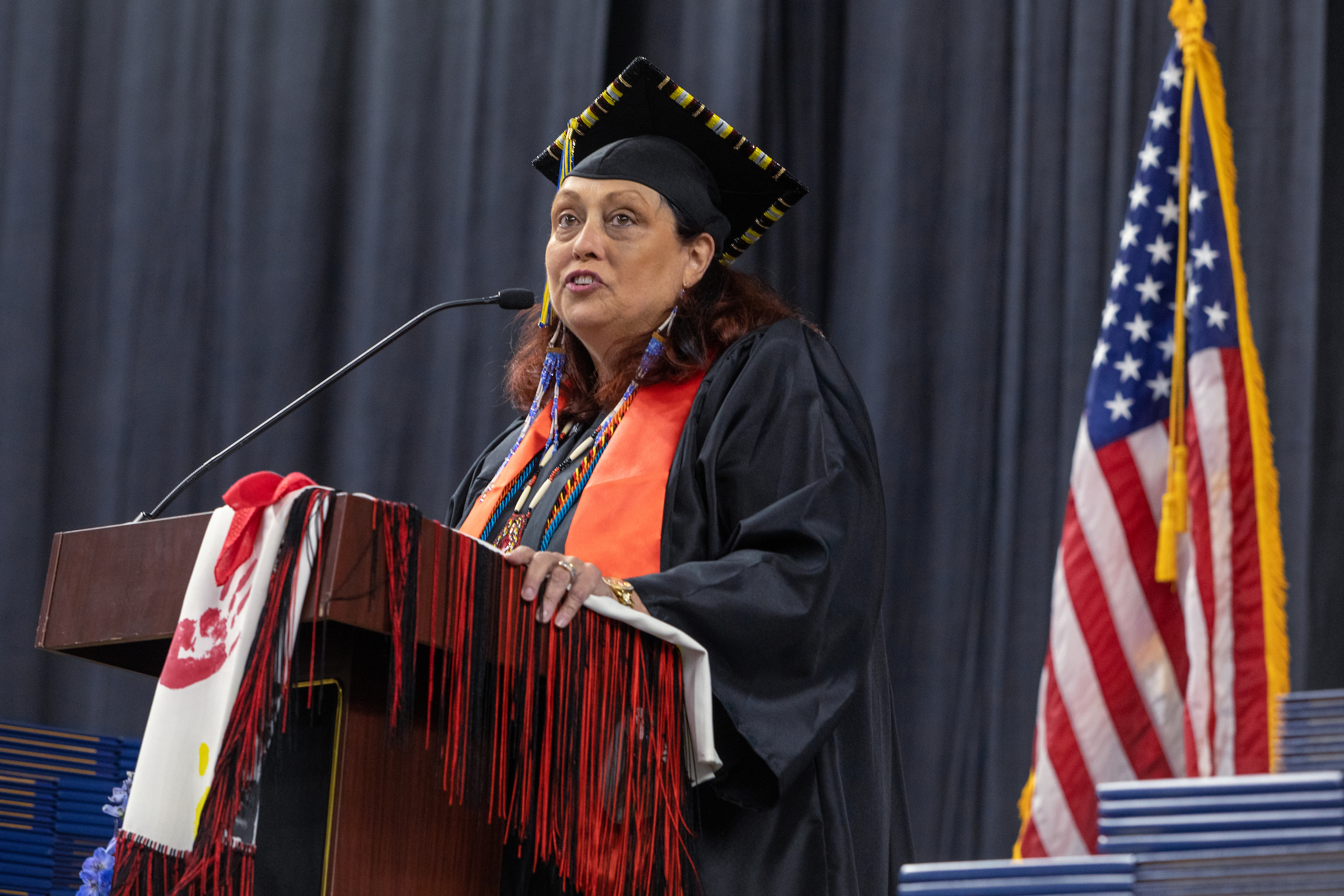 A woman in university regalia speaks at a podium