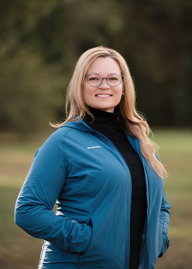 Portrait of a blond woman with glasses, a black shirt and blue jacket outdoors