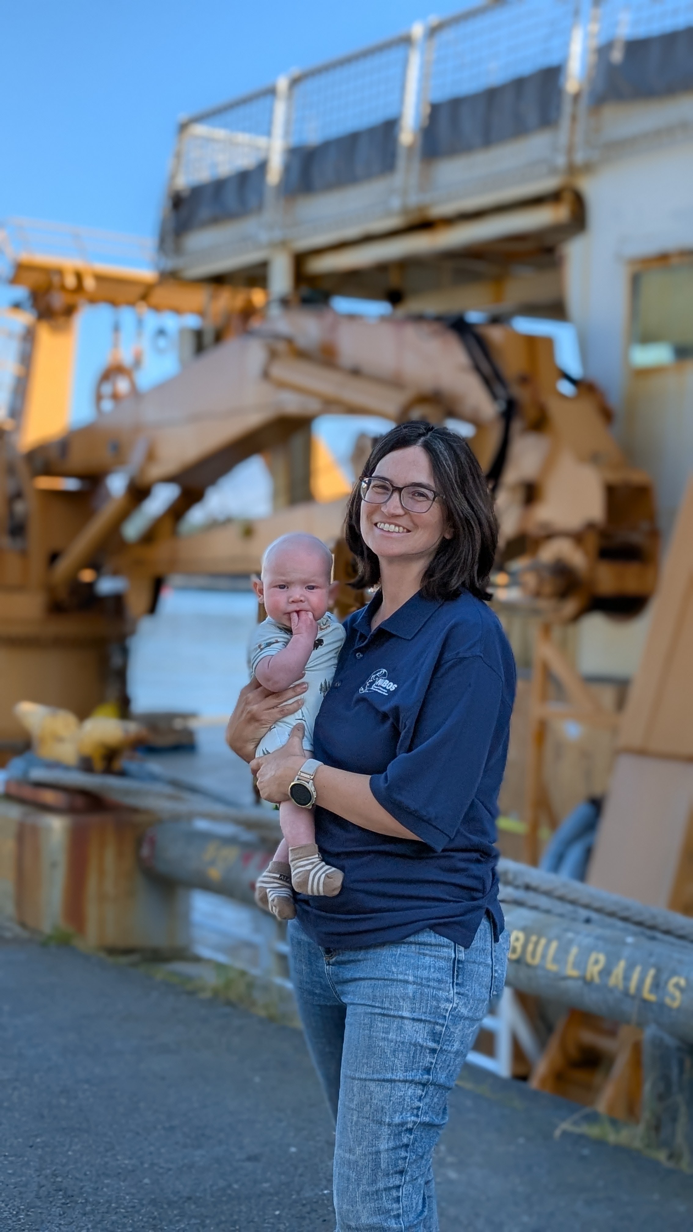 A researcher holds a baby in front of a ship.