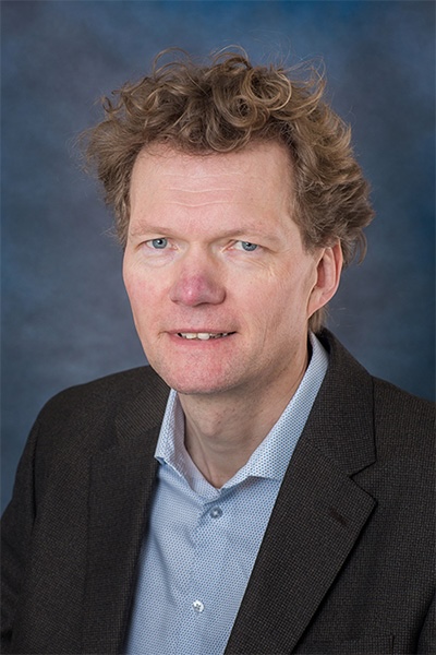 A portrait shows a man with curly, orange hair wearing a blue dress shirt and a suit jacket.