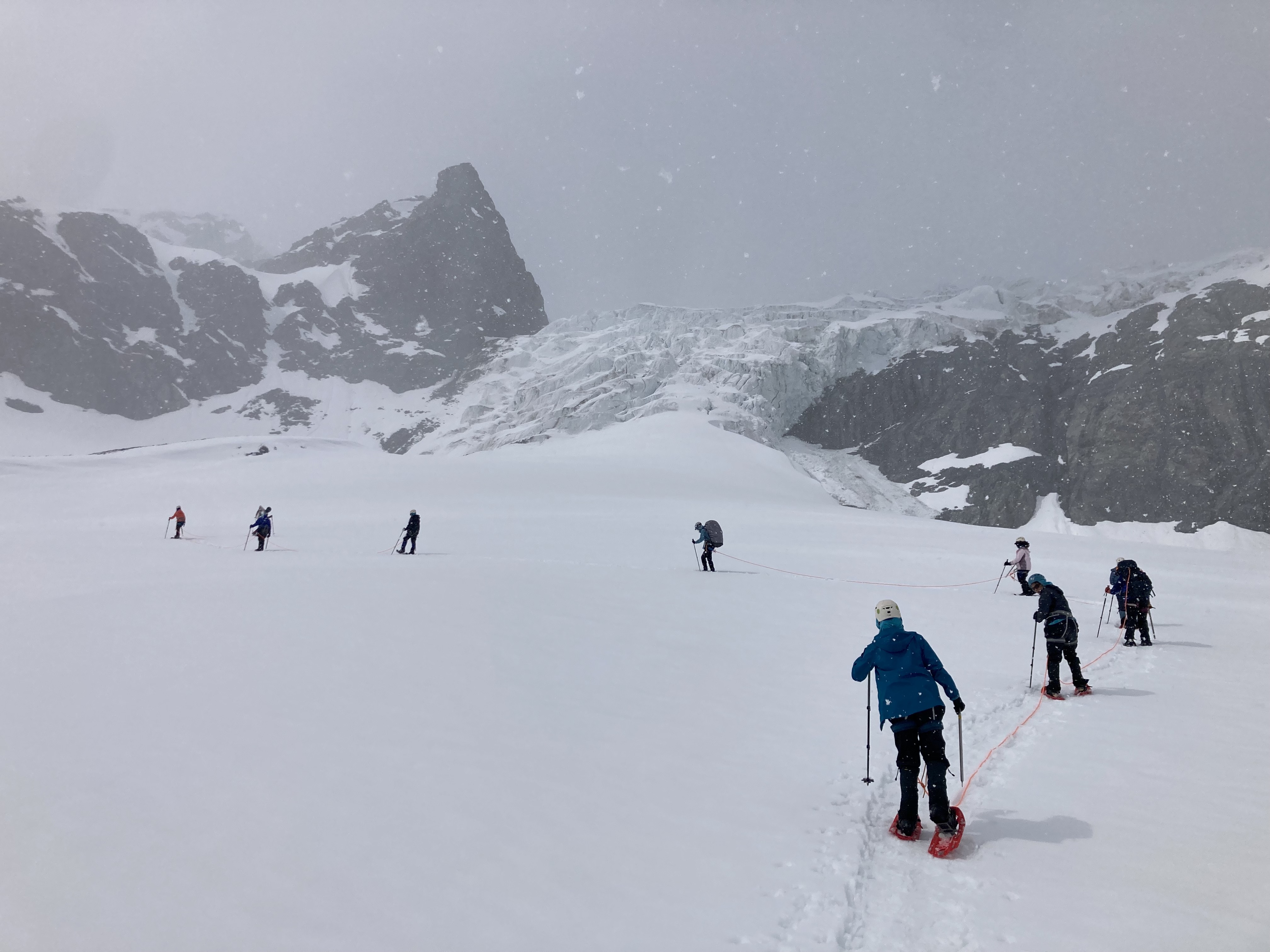 A group of young women traverse a snow field on a rope line in front of Gulkana Glacier in the Alaska Range.