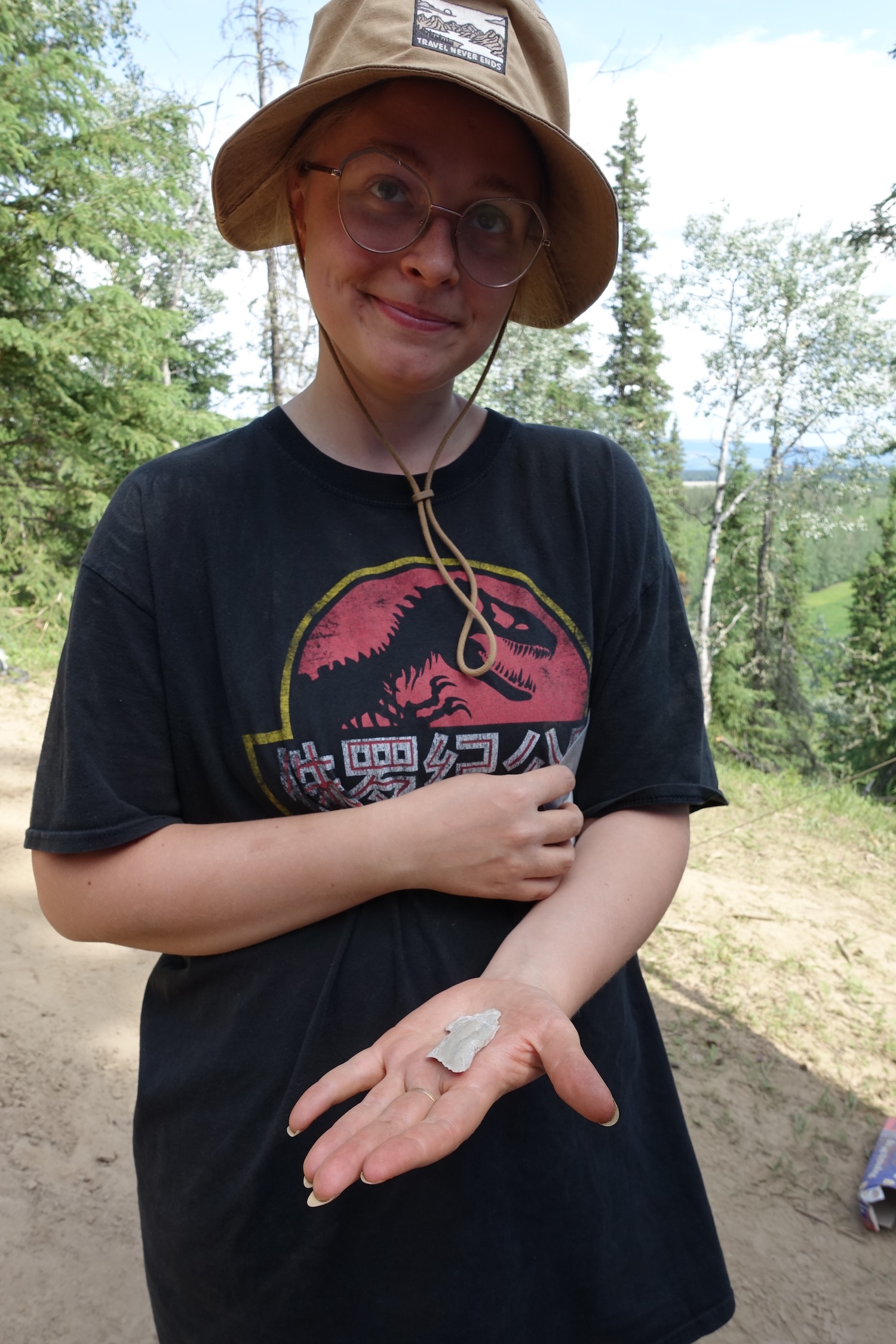 A woman in a brimmed hat and black T-shirt holds a piece of light-colored rock before her in the palm of one hand. 