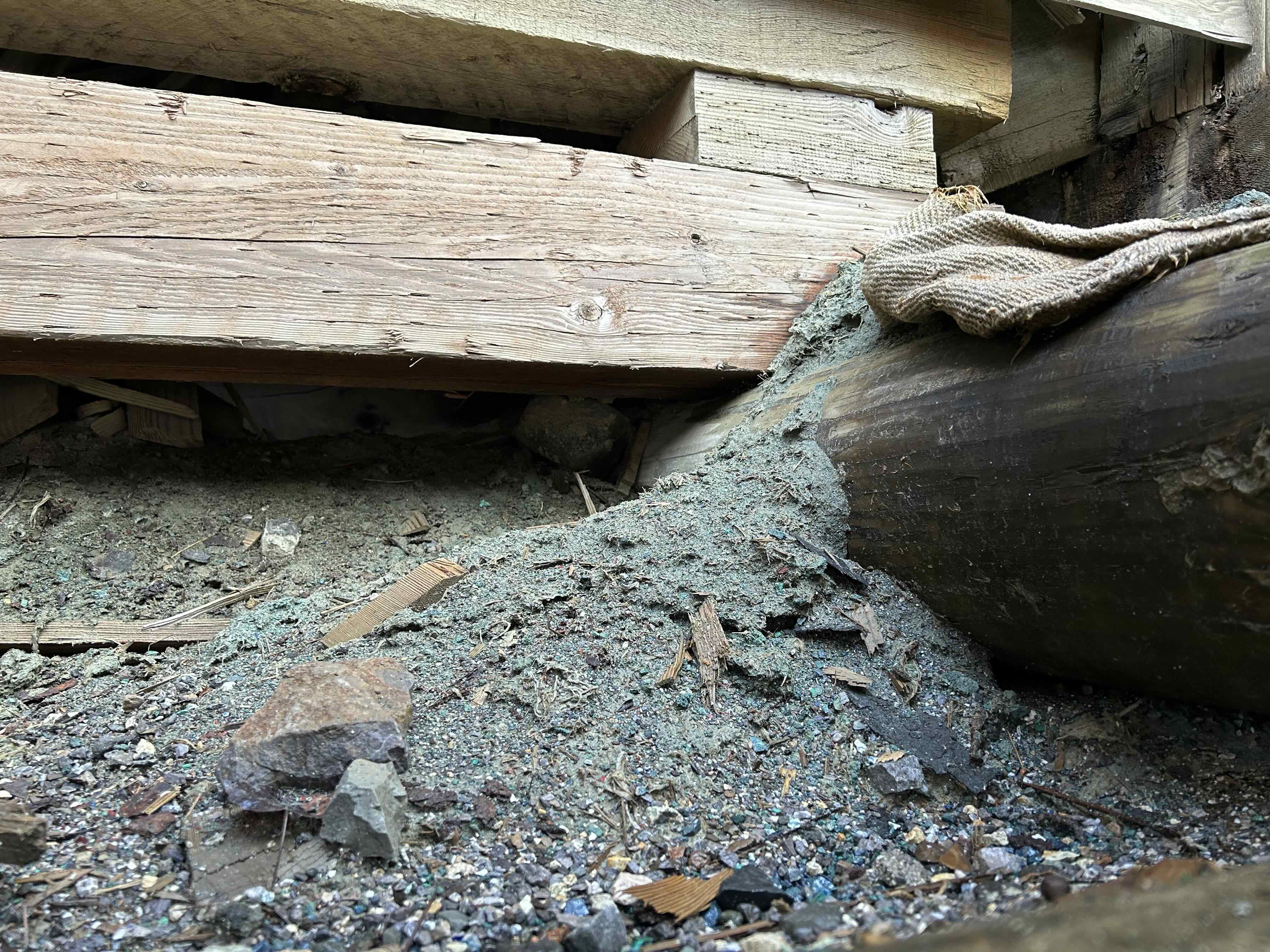 Fine greenish-blue mineral dust and larger particles from ore processing lie beneath wooden timbers at the front of the Kennecott Mill, apparently spilled from a shipping bag. The finished copper product was bagged here for shipment by rail.