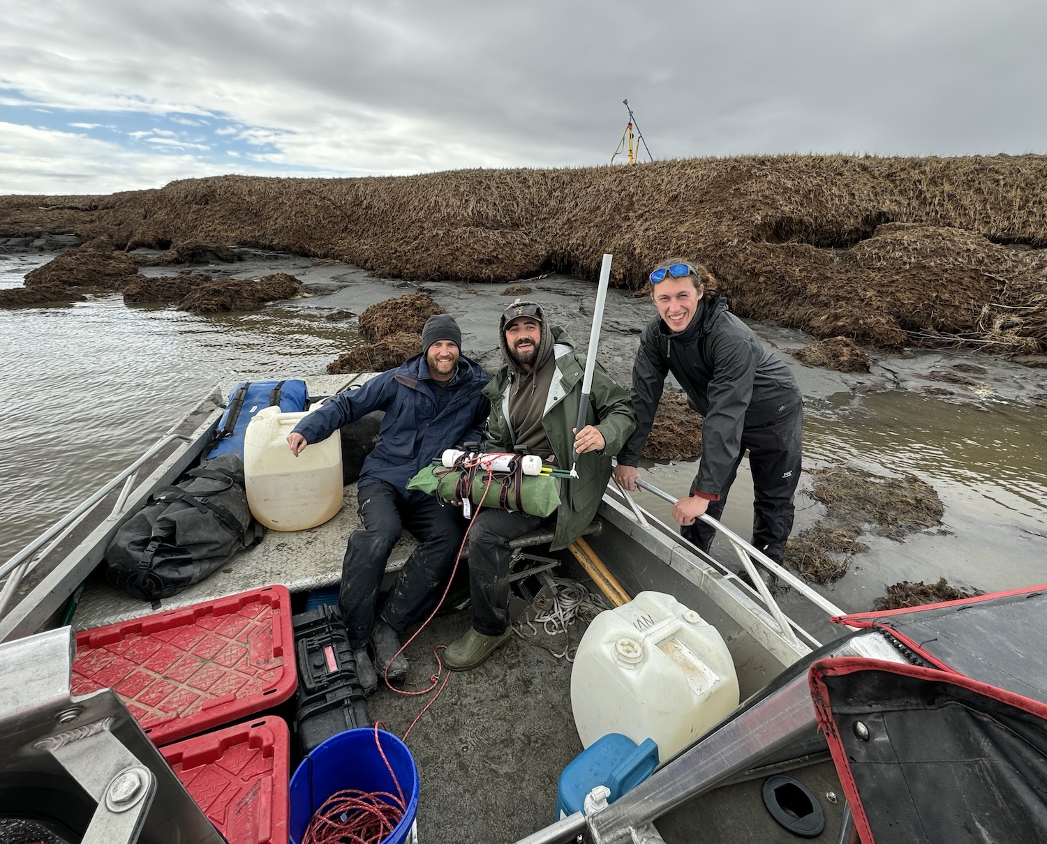 Three people gather around the bow of a beached boat.