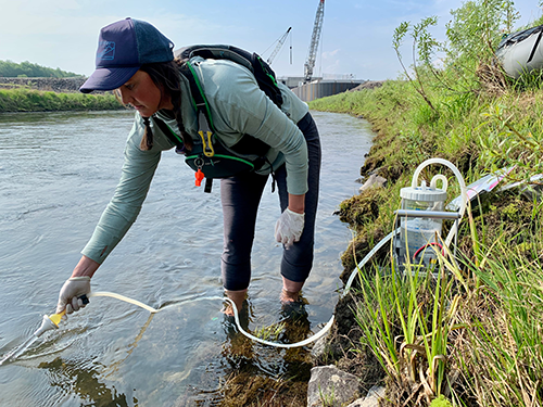 AK CASC graduate student Maggie Harings wears waders while sampling water with a scientific instrument in a river.