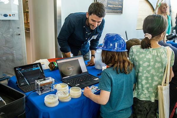 A scientist (man) in a blue shirt talks to young visitors at the Arctic Research Open House in 2023.
