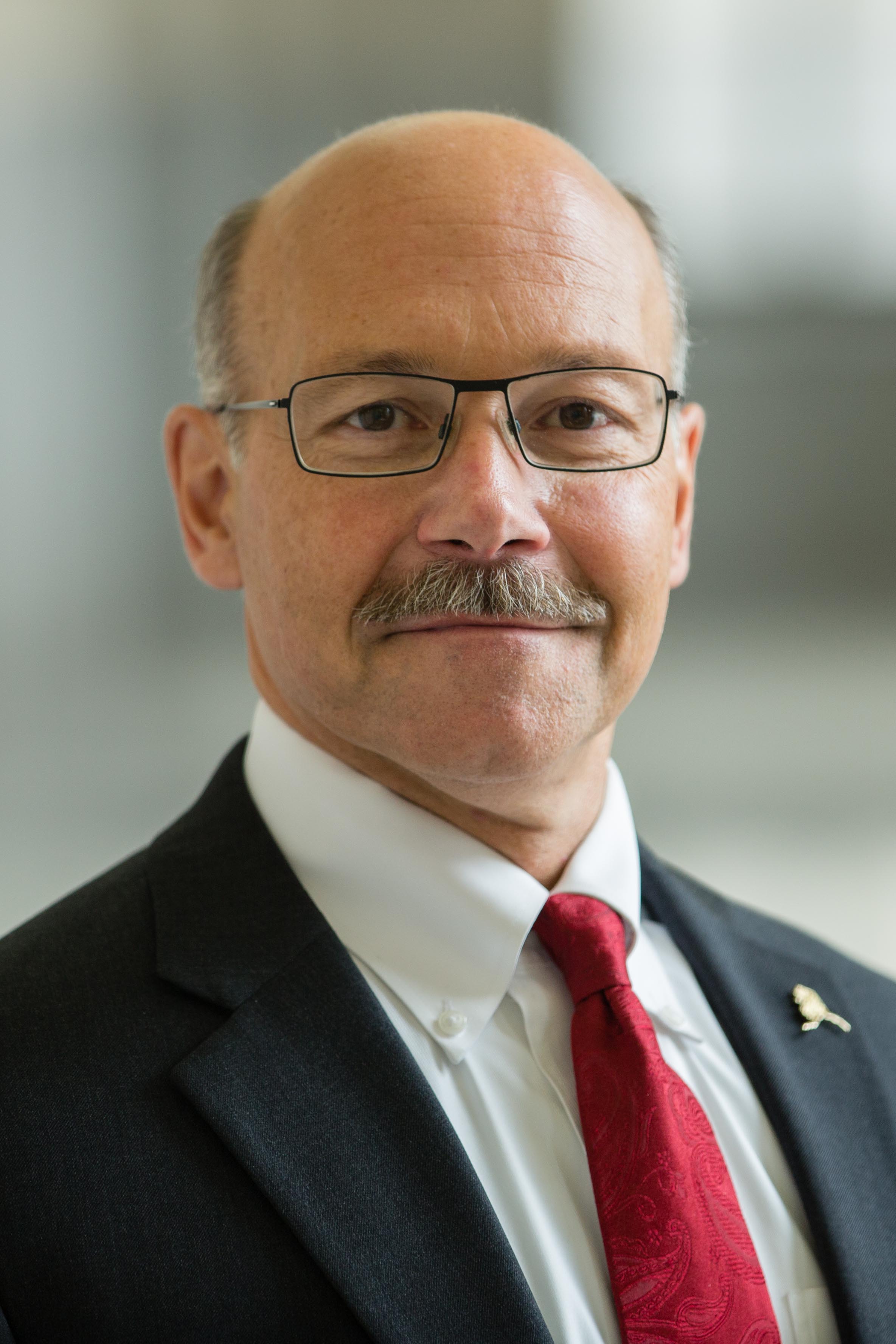 A man wearing a white shirt, red tie and dark colored business jacket.