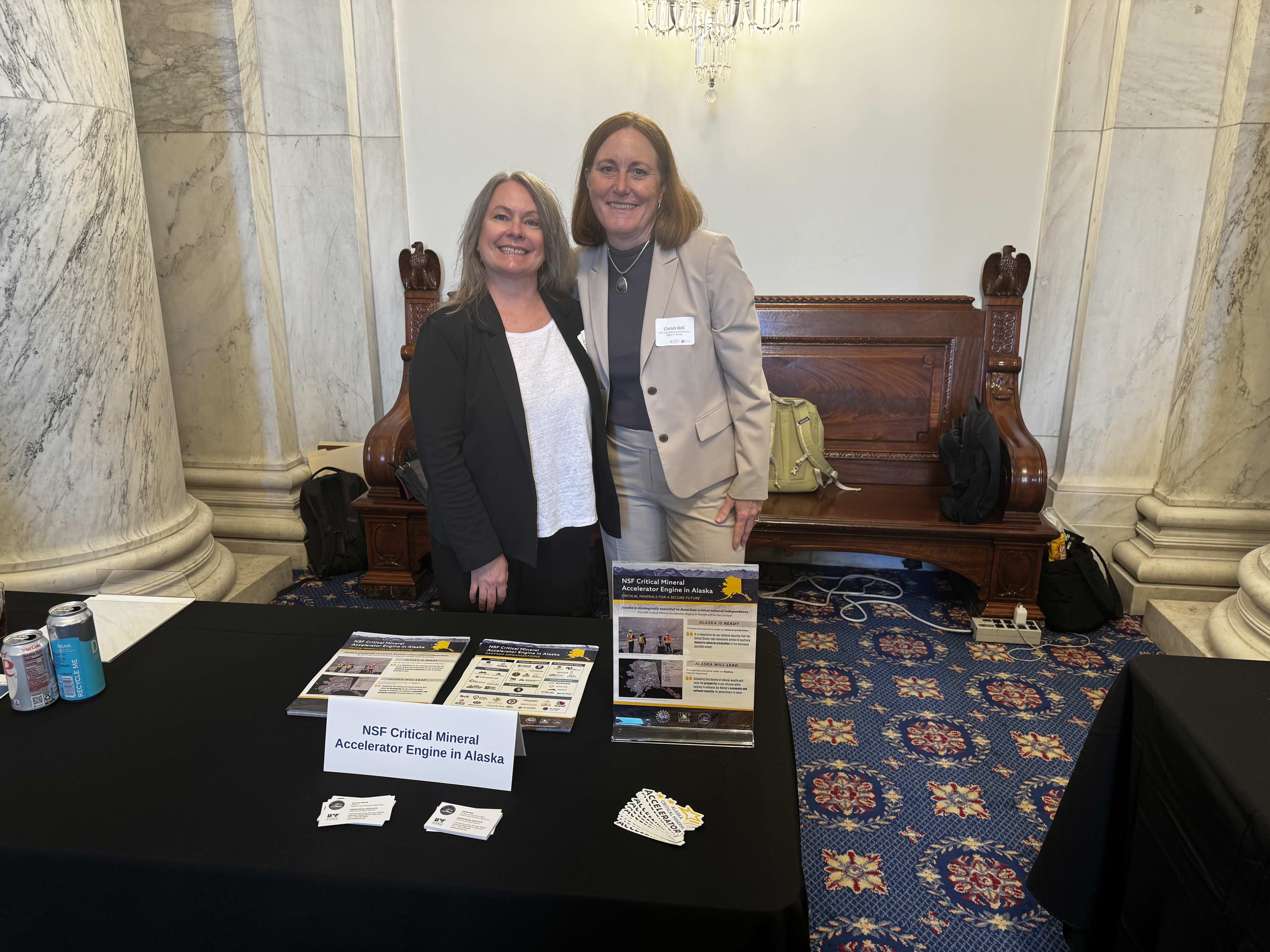 Two smiling people stand behind a table with pamphlets on it. 