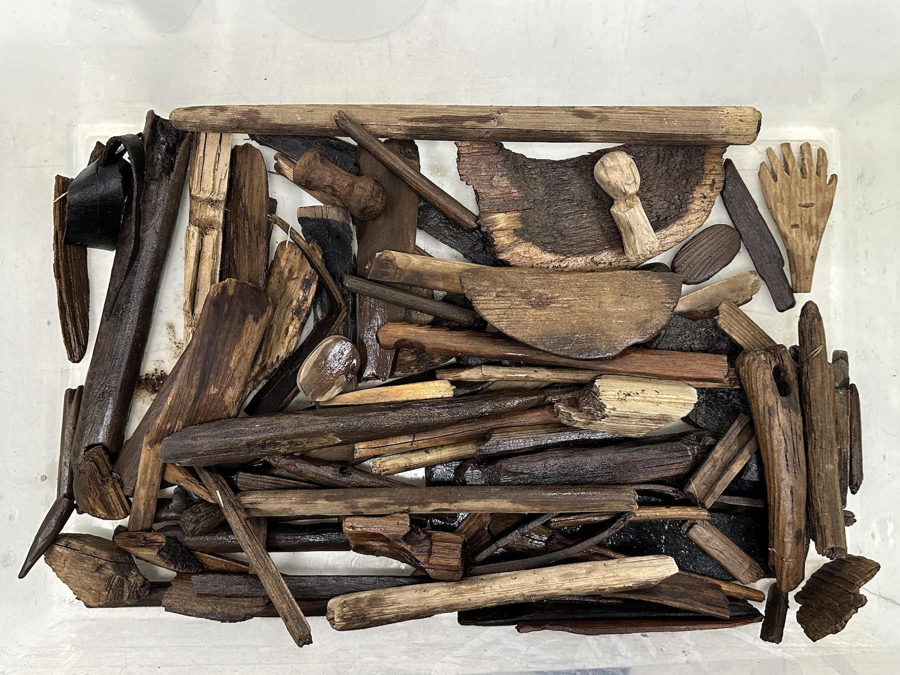 Wooden artifacts fill the bottom of a rectangular white plastic tub.