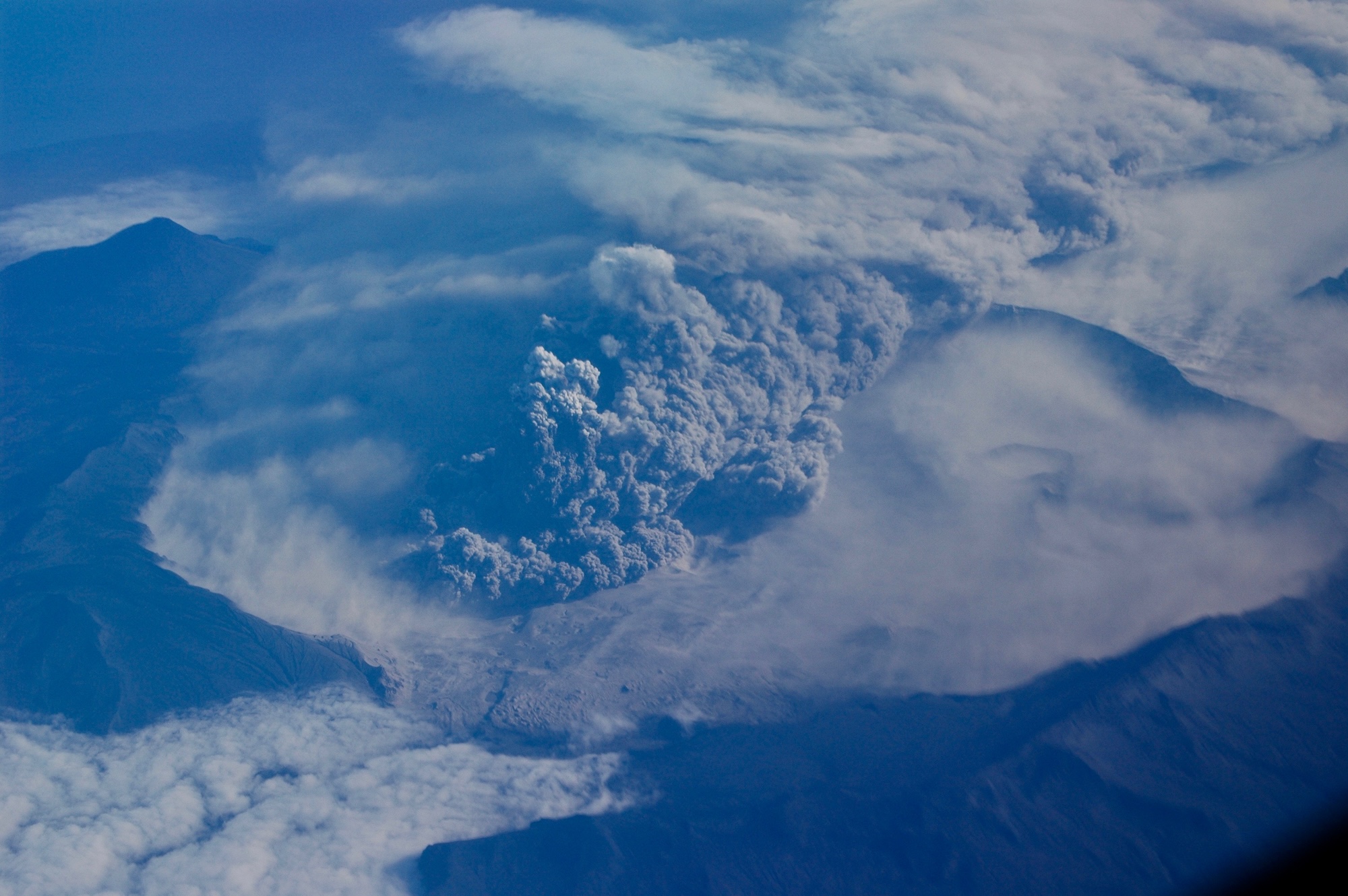An ash cloud boils from an erupting volcano, as viewed from an aircraft high above.