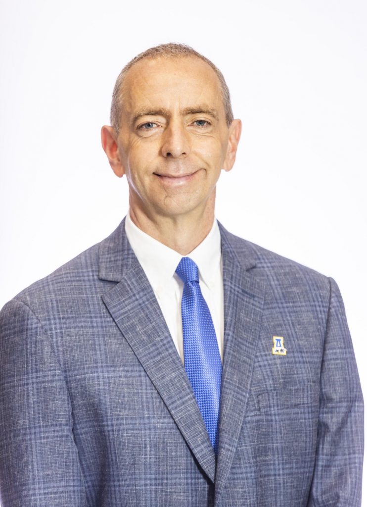 A smiling man wearing a gray suit and blue tie.