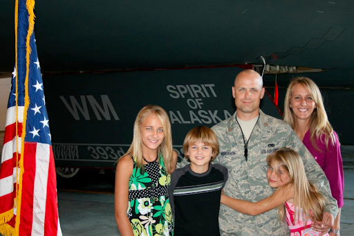 A military family poses for a photo in front of an aircraft.