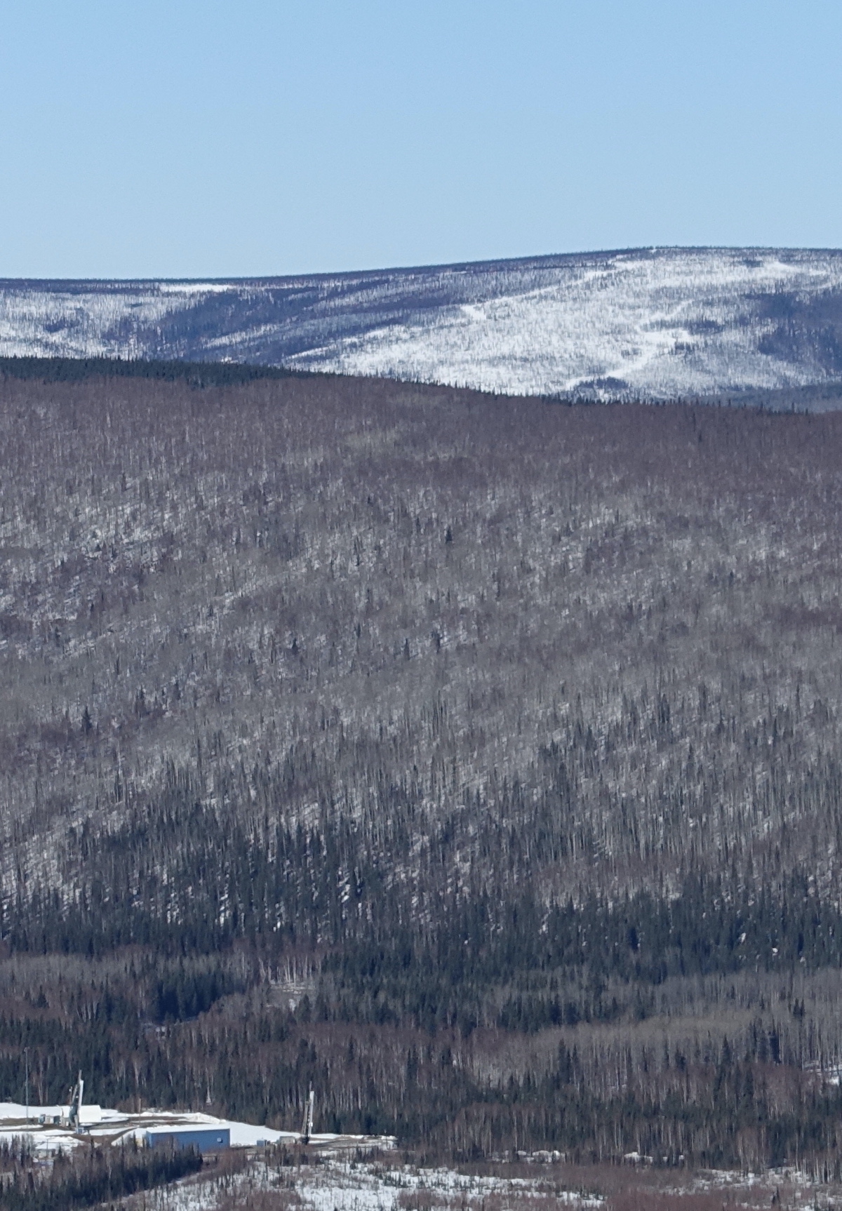 Two rockets sit upright in the bottom of a valley between tree-covered, snowy hills.