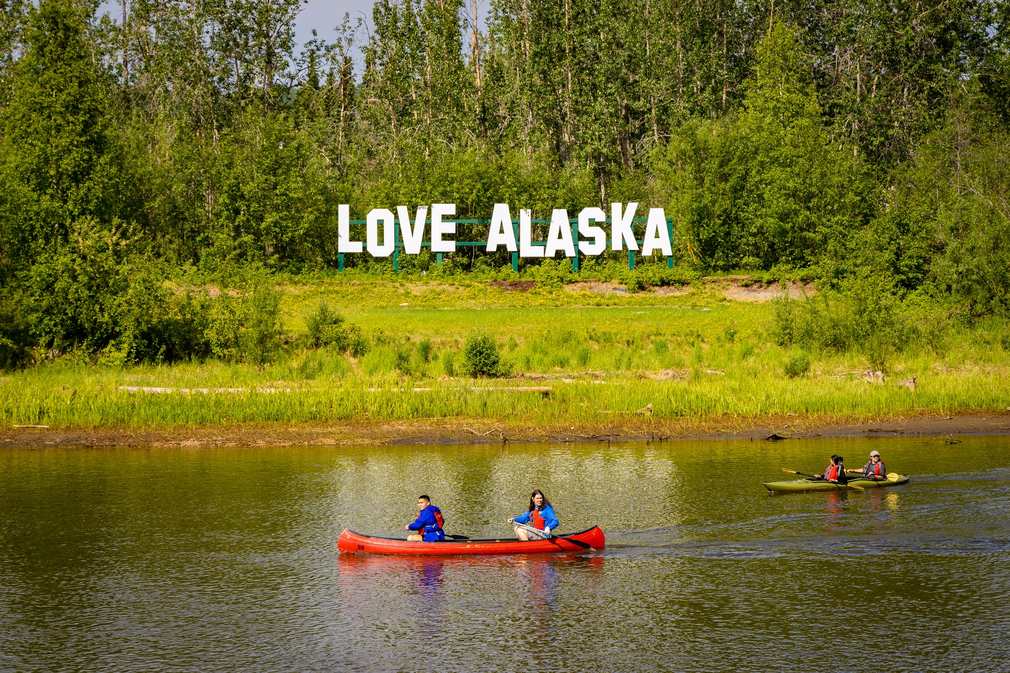 Students canoeing on the Chena River in front of the Love Alaska sign