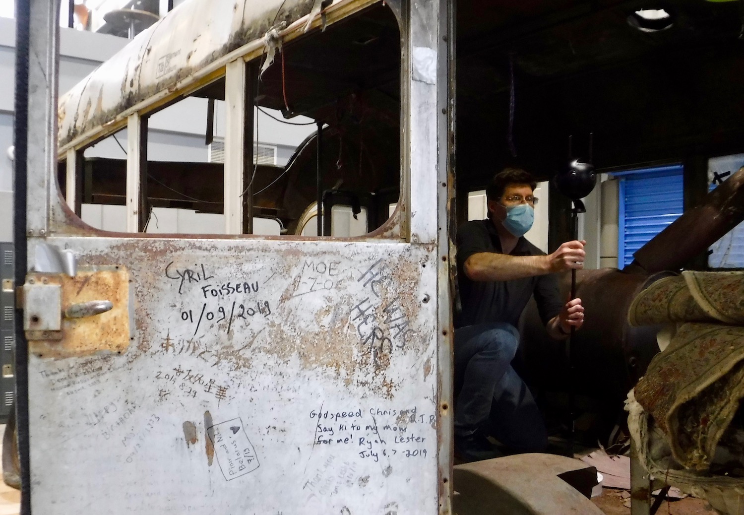 A man holds a visual recording device on a stick inside a disheveled bus.