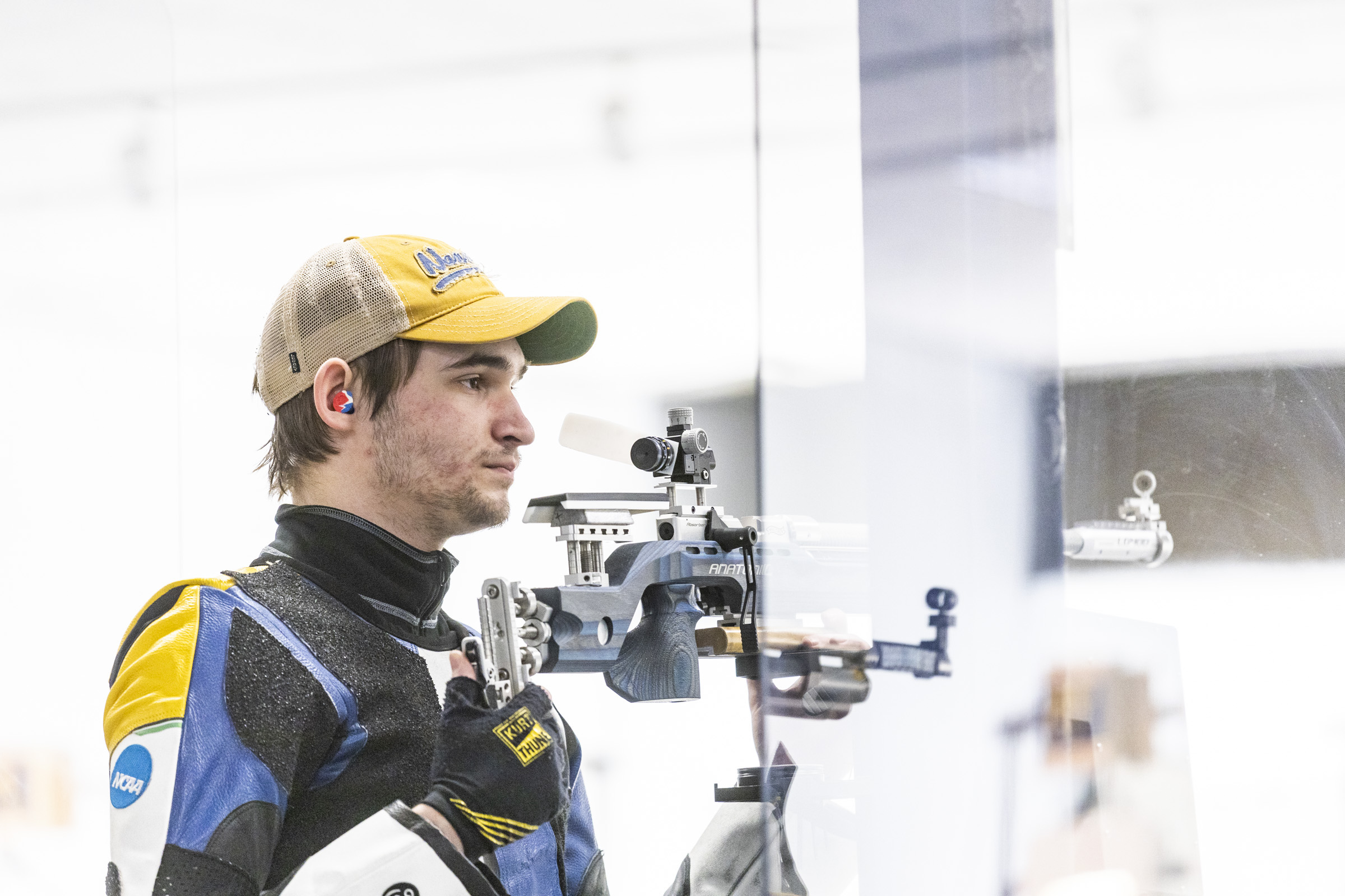 A man in UAF blue and gold competition shooting gear holds a rifle.
