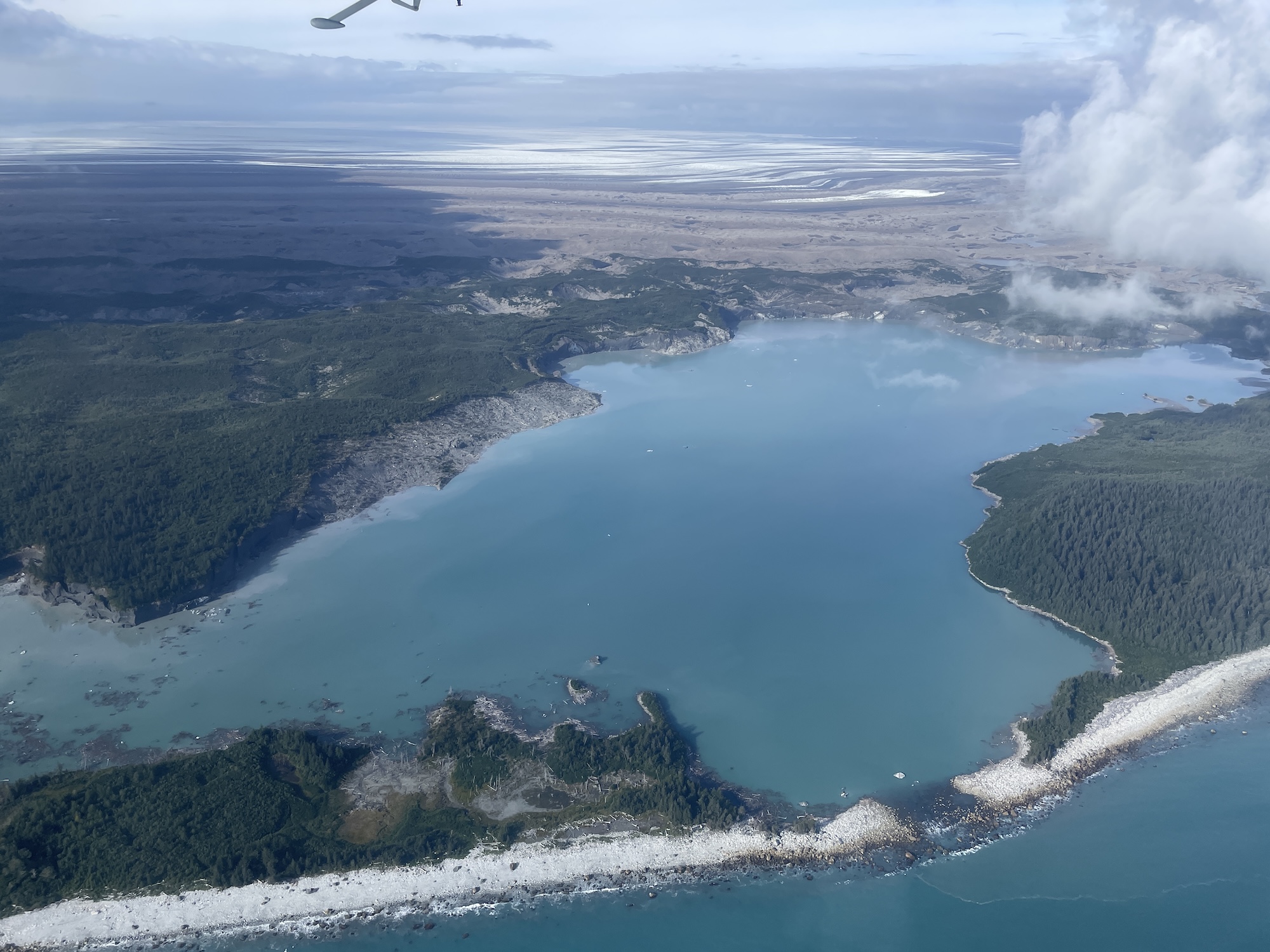 A lake sits between a low, flat glacier and the ocean.