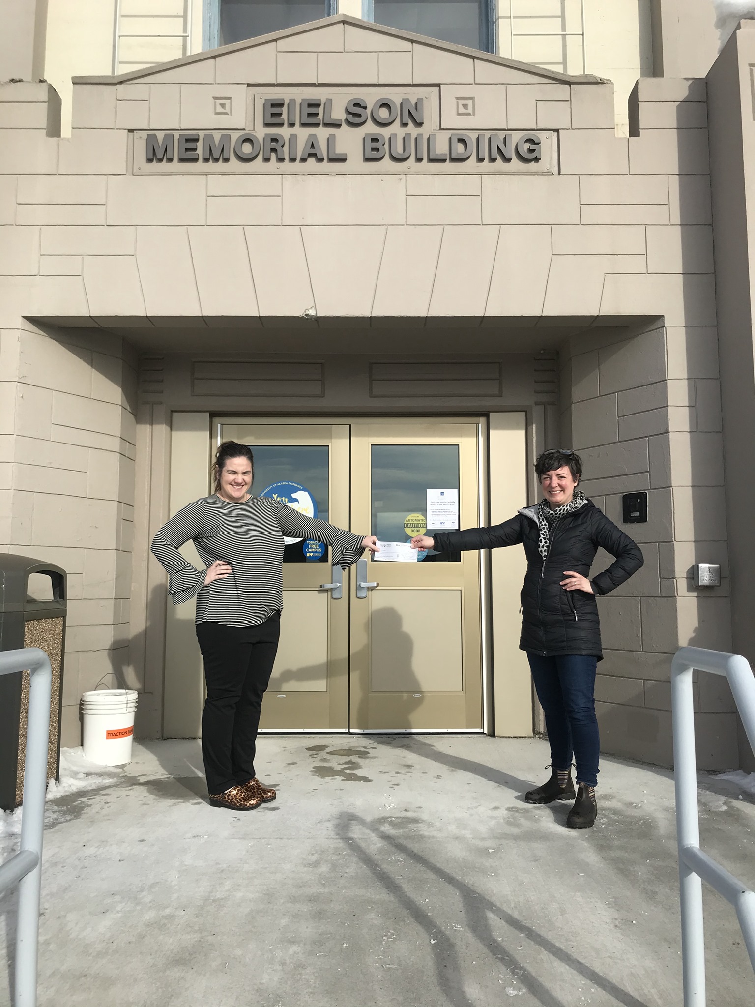 Two women hold a check outside a building