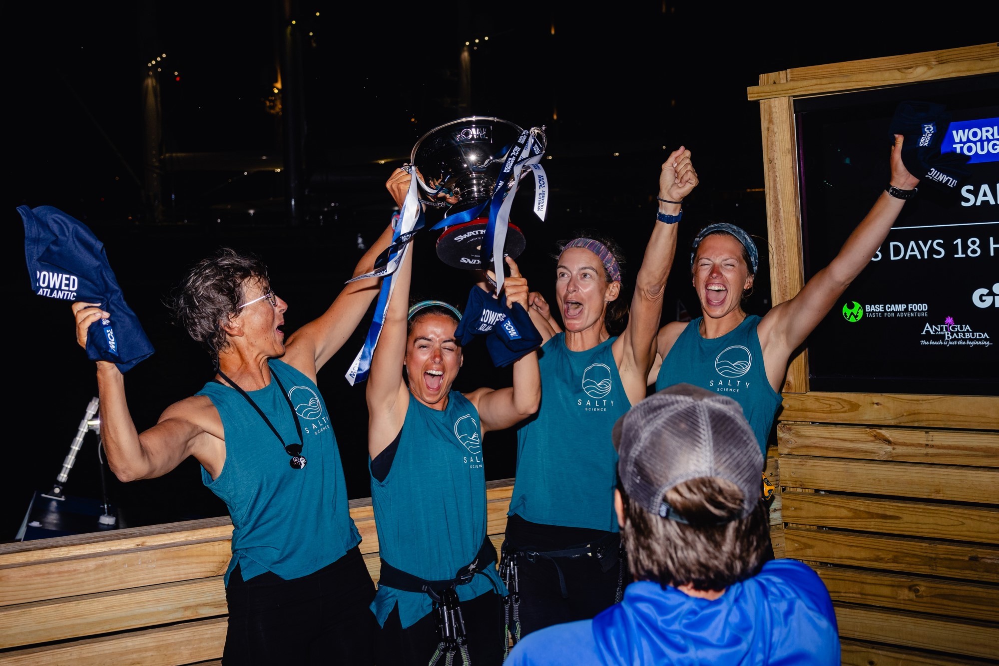 Four women shout, raise their hands in the air and lift a ribbon-adorned silver trophy cup.
