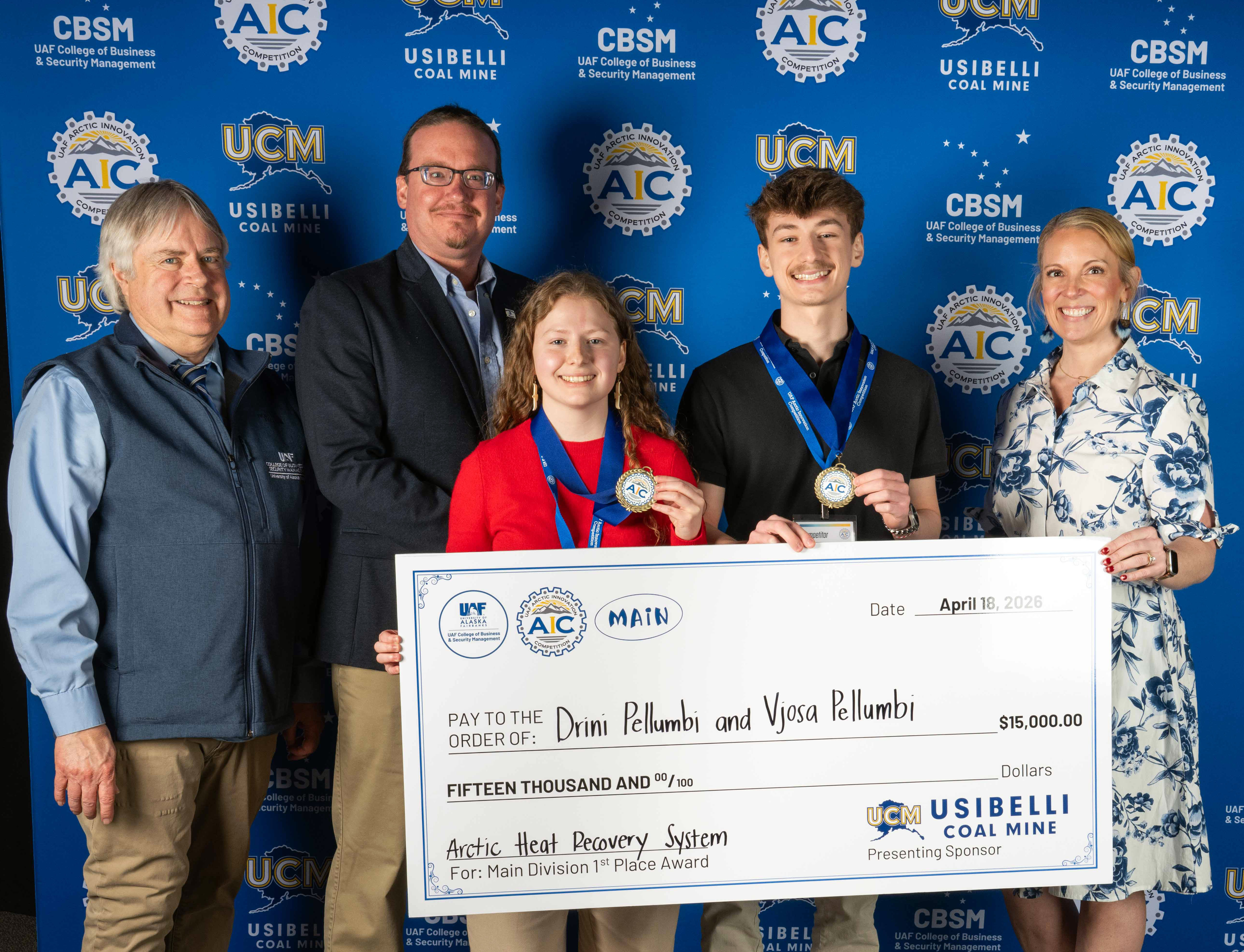 Vjosa and Drini Pellumbi pose with a group of people. They hold an oversized presentation check for $15,000 from Usibelli Coal Mine and show off their award medals.