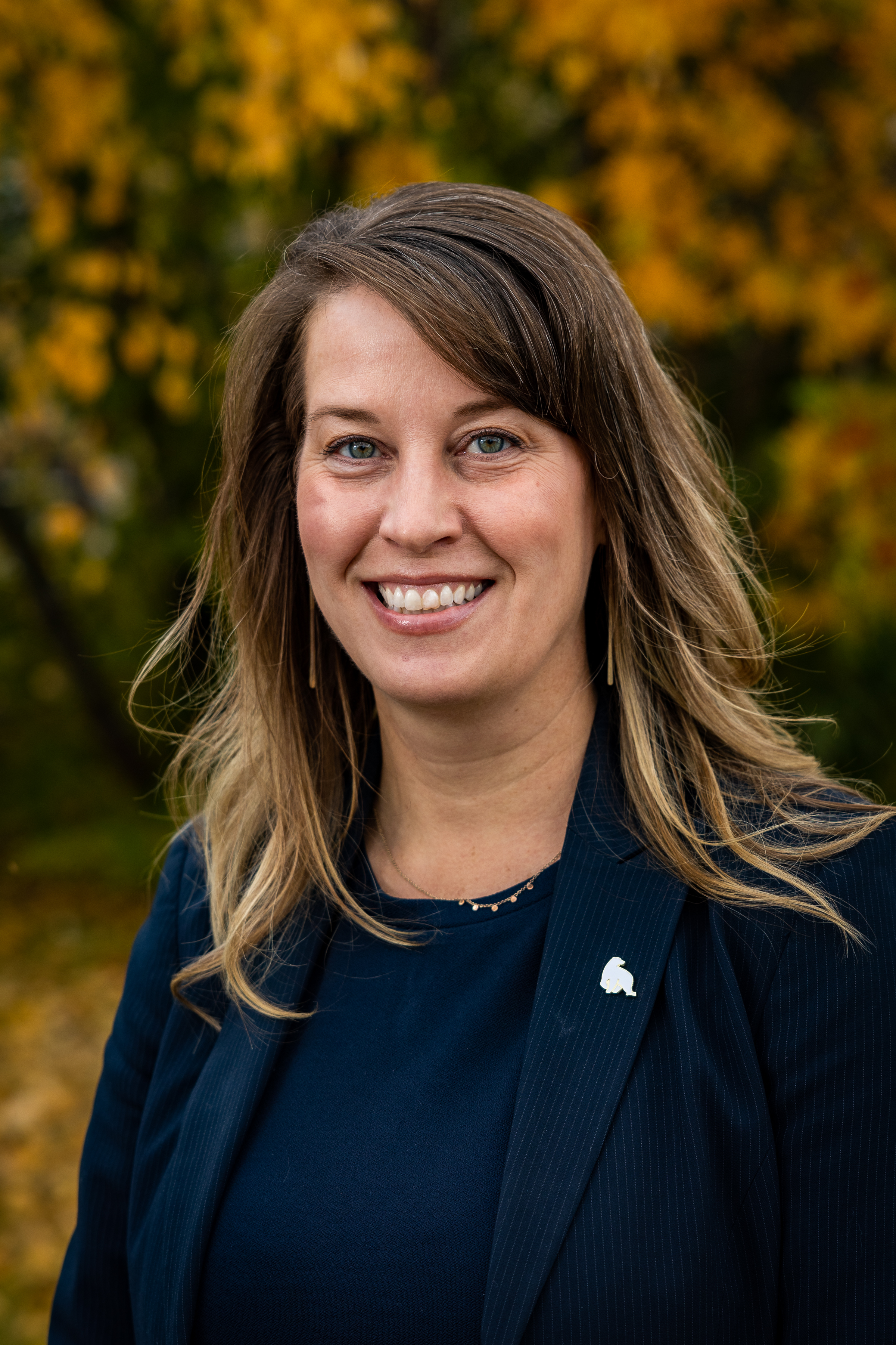 A woman with a dark blue shirt and a blazer with a polar bear pin.