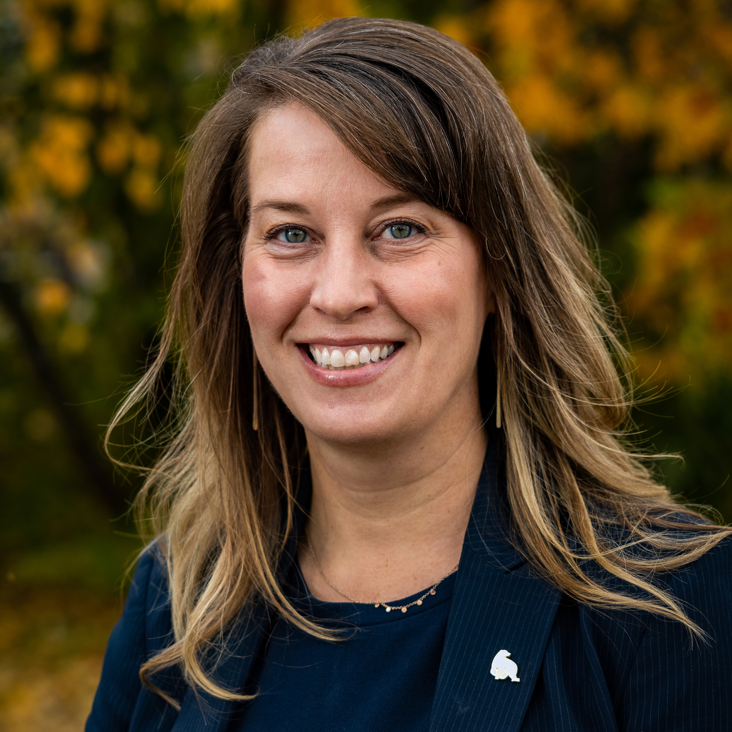 A woman with a dark blue shirt and a blazer with a polar bear pin.