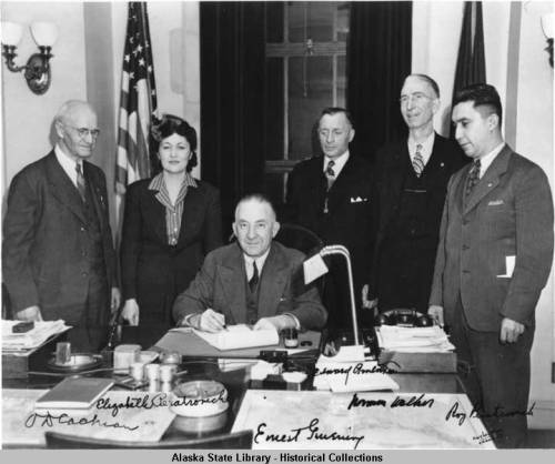Governor Gruening (seated) signs the anti-discrimination act of 1945. Witnessing the signing are (left to right) O. D. Cochran, Elizabeth Peratrovich,  Edward Anderson, Norman Walker, and Roy Peratrovich.