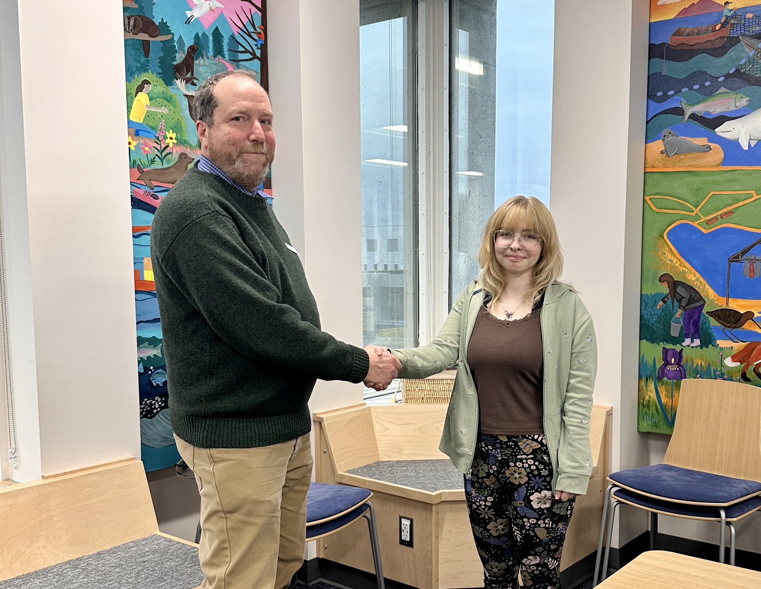 A man and woman shake hands and smile for the camera.