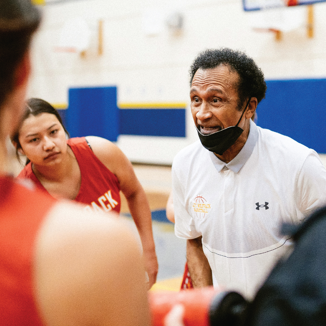 an older Black man stands on a basketball court coaching a girls' team