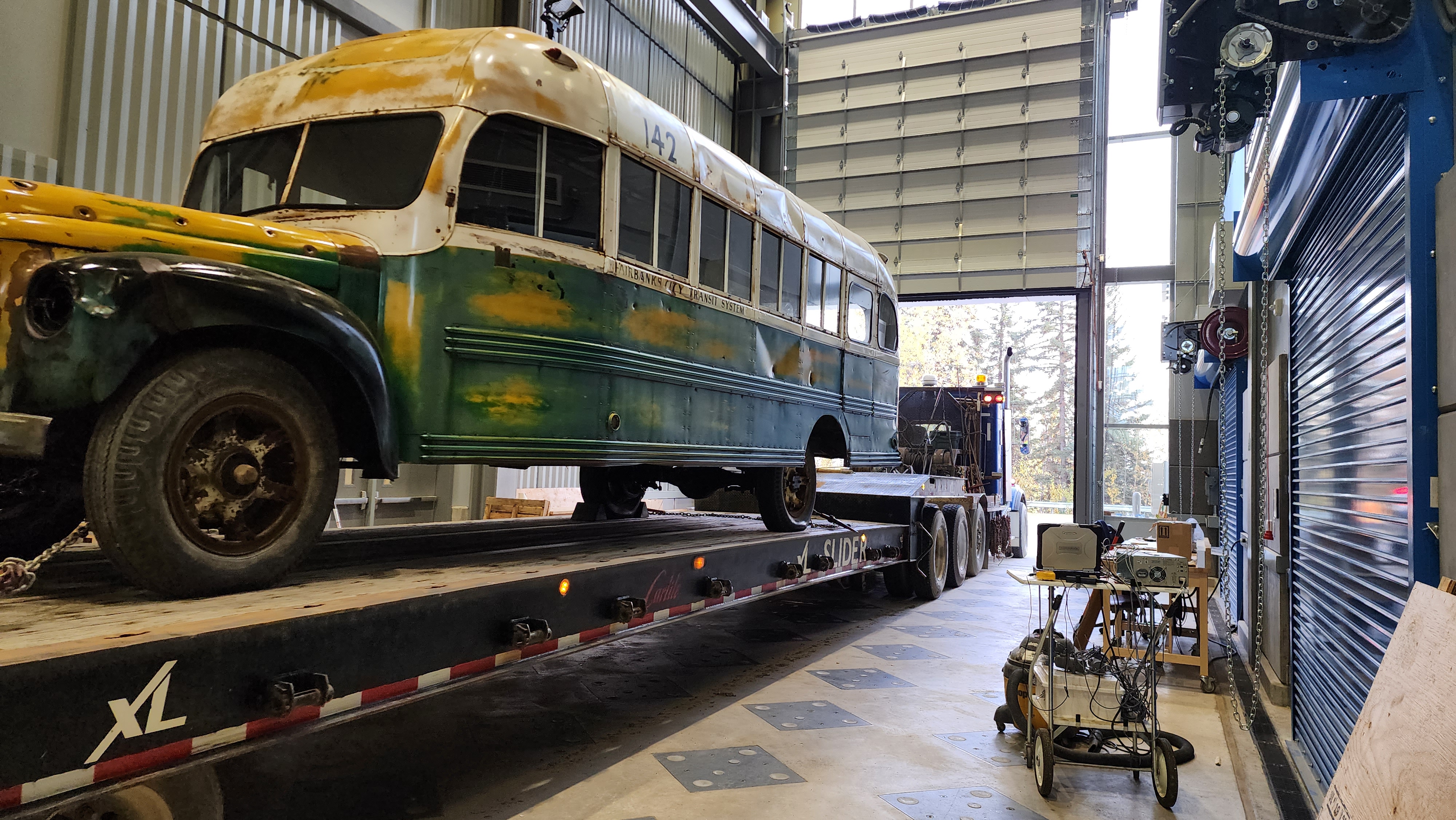 Bus 142 sits on a flatbed inside a large workshop bay.