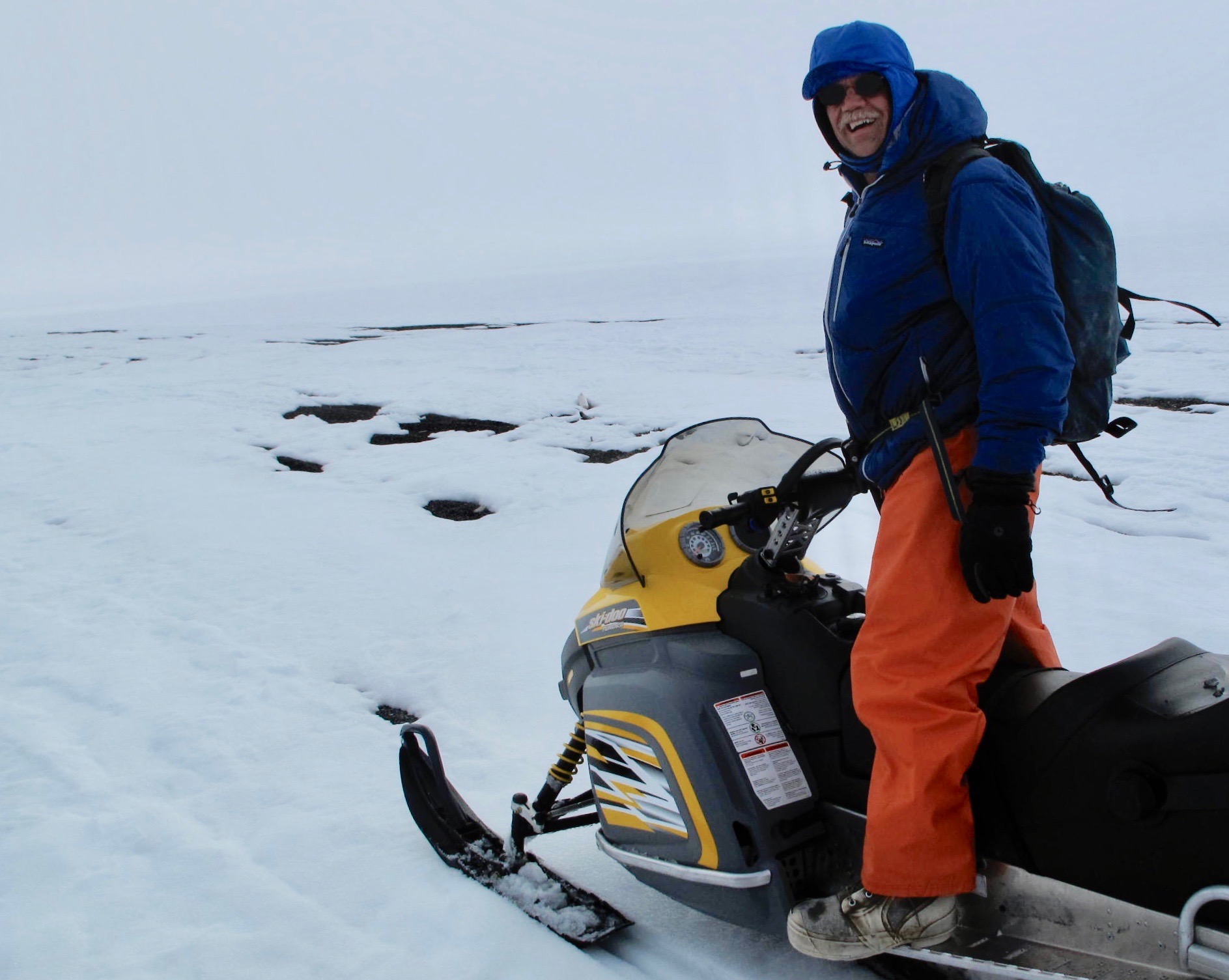 A man in winter gear stands on a snowmachine on an expanse of snowy sea ice.