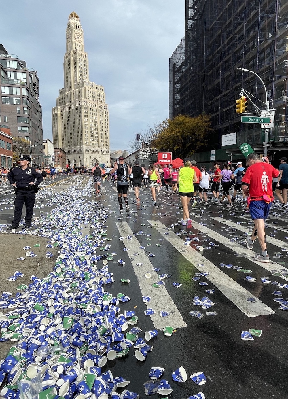 Discarded paper cups cover part of a street as marathon runners pass by.