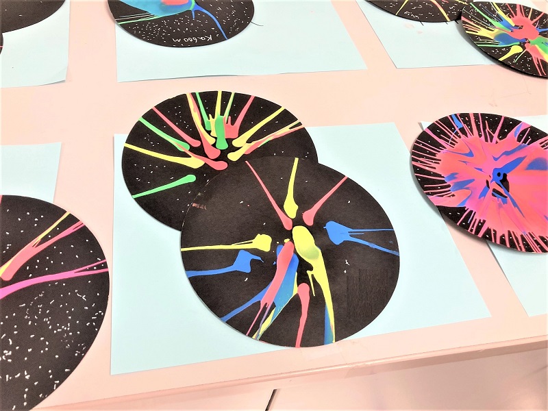 black paper circles with splashes of brightly colored paint laid out on a table