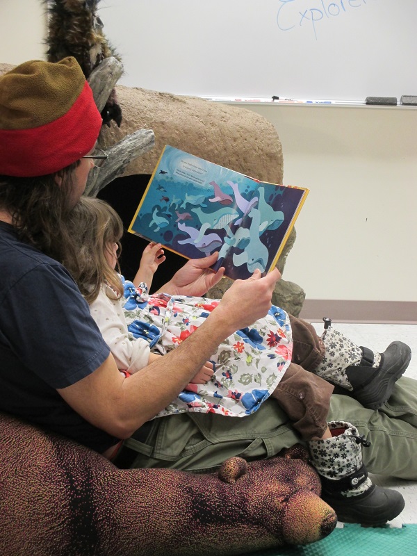 a child sits in an adult's lap and holds a storybook they're reading together