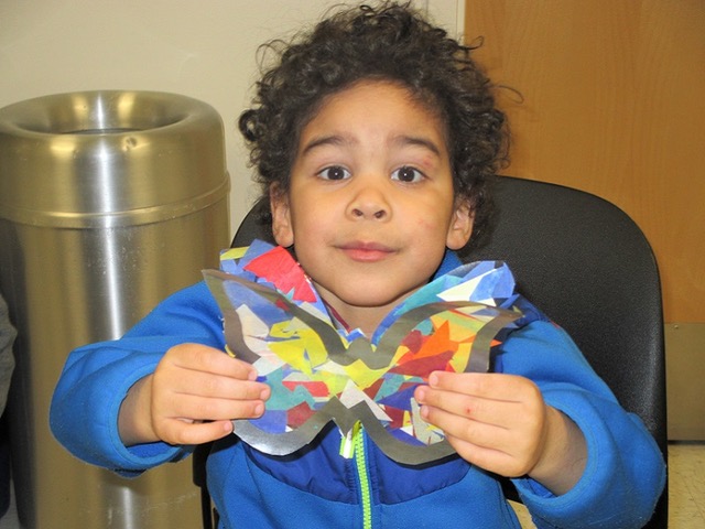 A small child holds up a butterfly crafted from paper