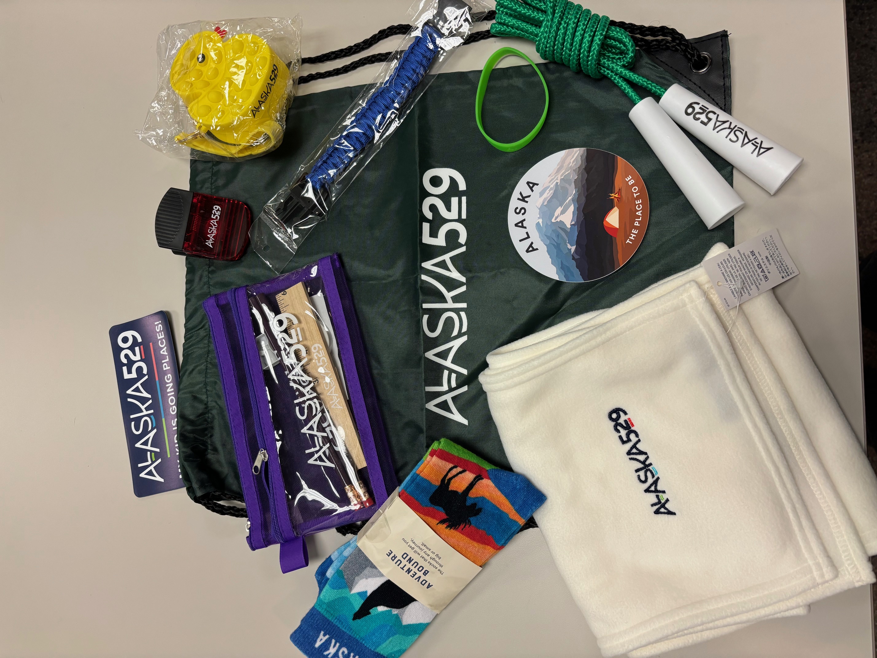 Grab bag items with Alaska 529 logo including stickers, a jump rope, pencil case, rubber duckie and scarf