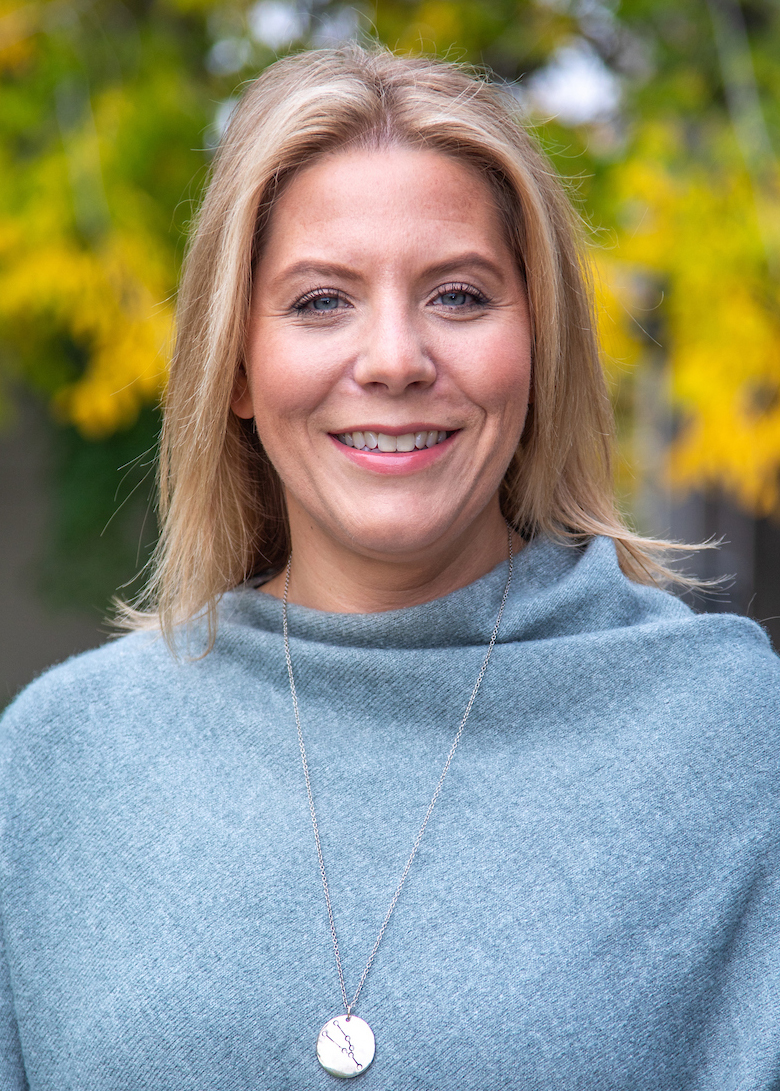 A woman wearing a light blue sweater outdoors in the fall.