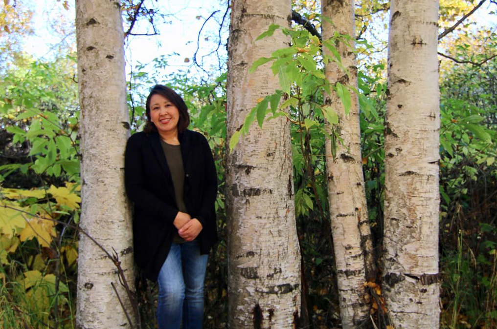 LaVerne Xilegg Demientieff standing among birch trees in the woods.