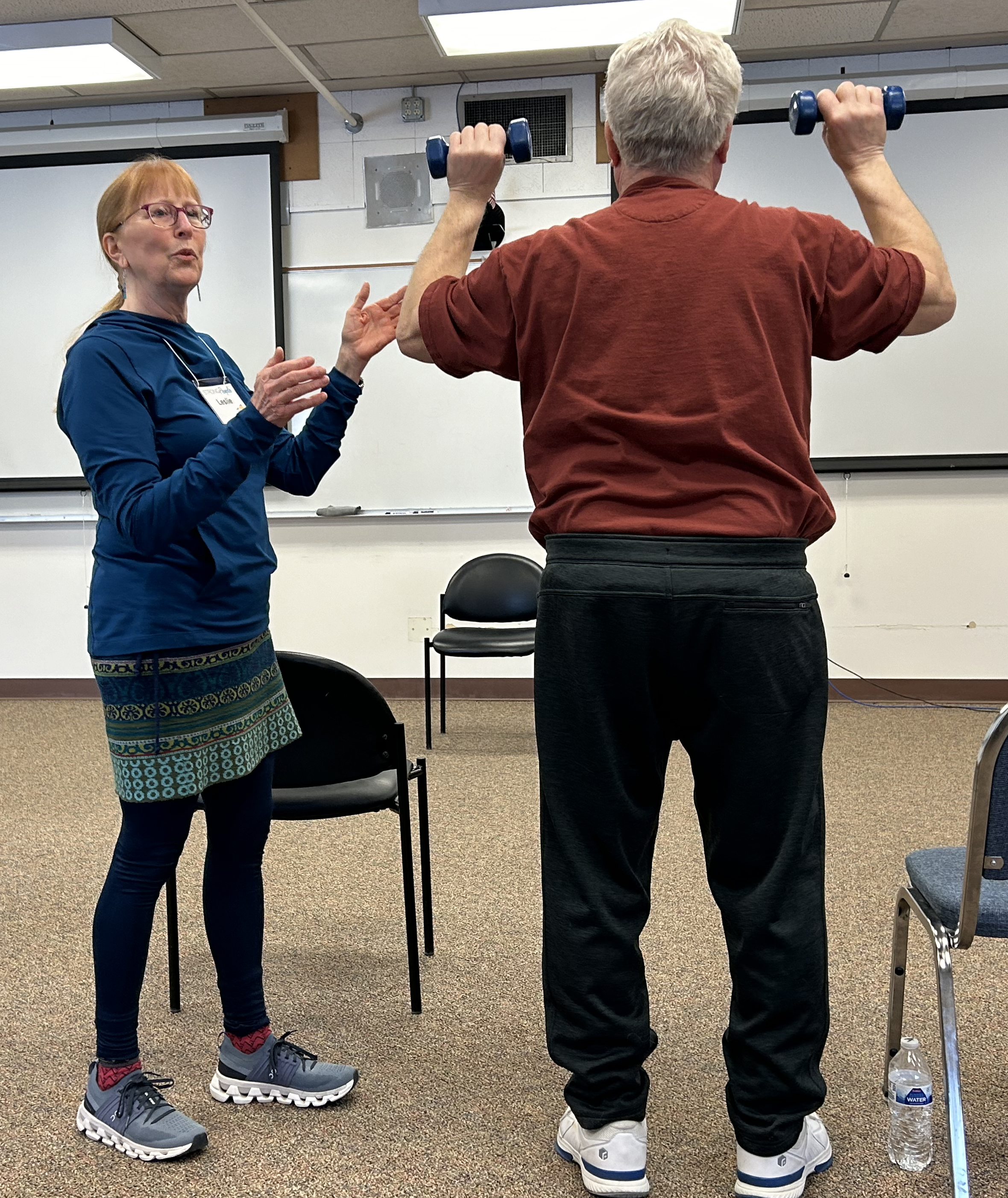 A woman coaches a man with weights in his hands in exercise.