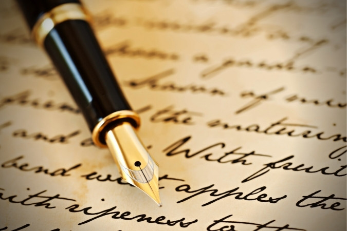 A calligraphy pen sits on top of yellowed paper covered in cursive script.