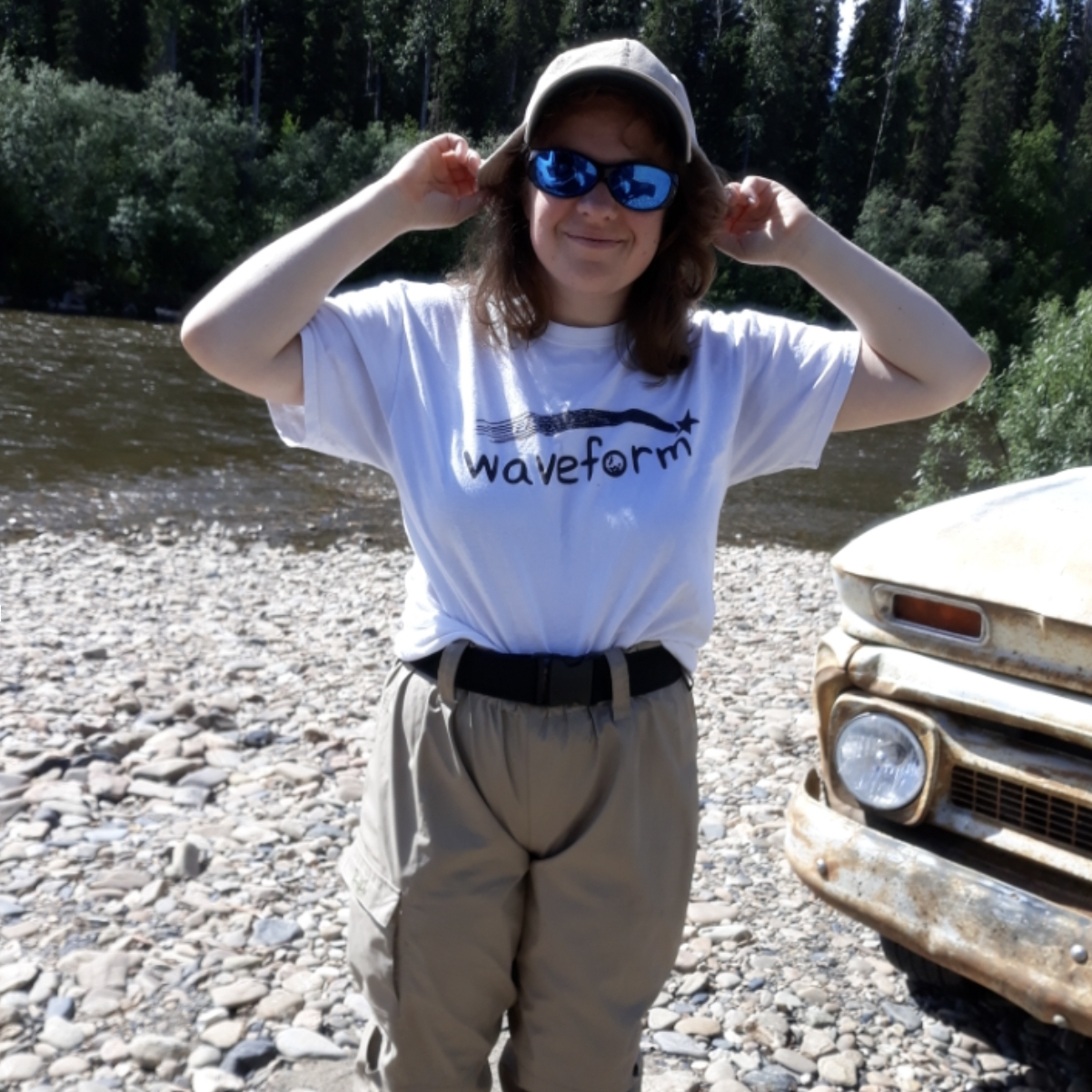 a woman wearing a fishing hat and waders by a pond