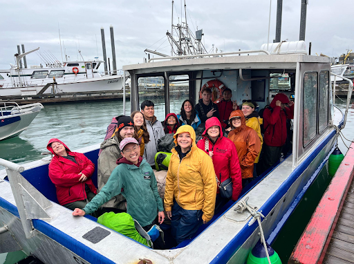 A group of people smiling and standing on a docked metal boat in the rain.