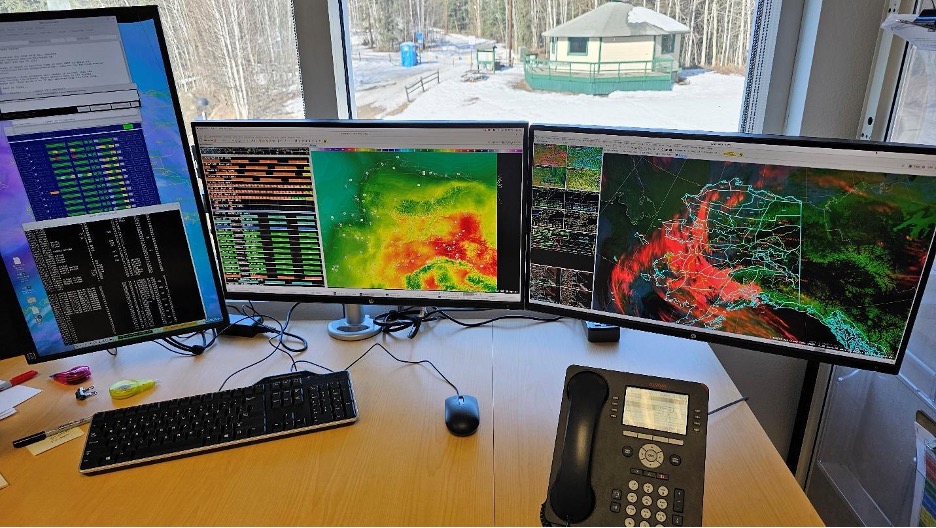 Two computer screens on a desk showing Alaska weather weather maps