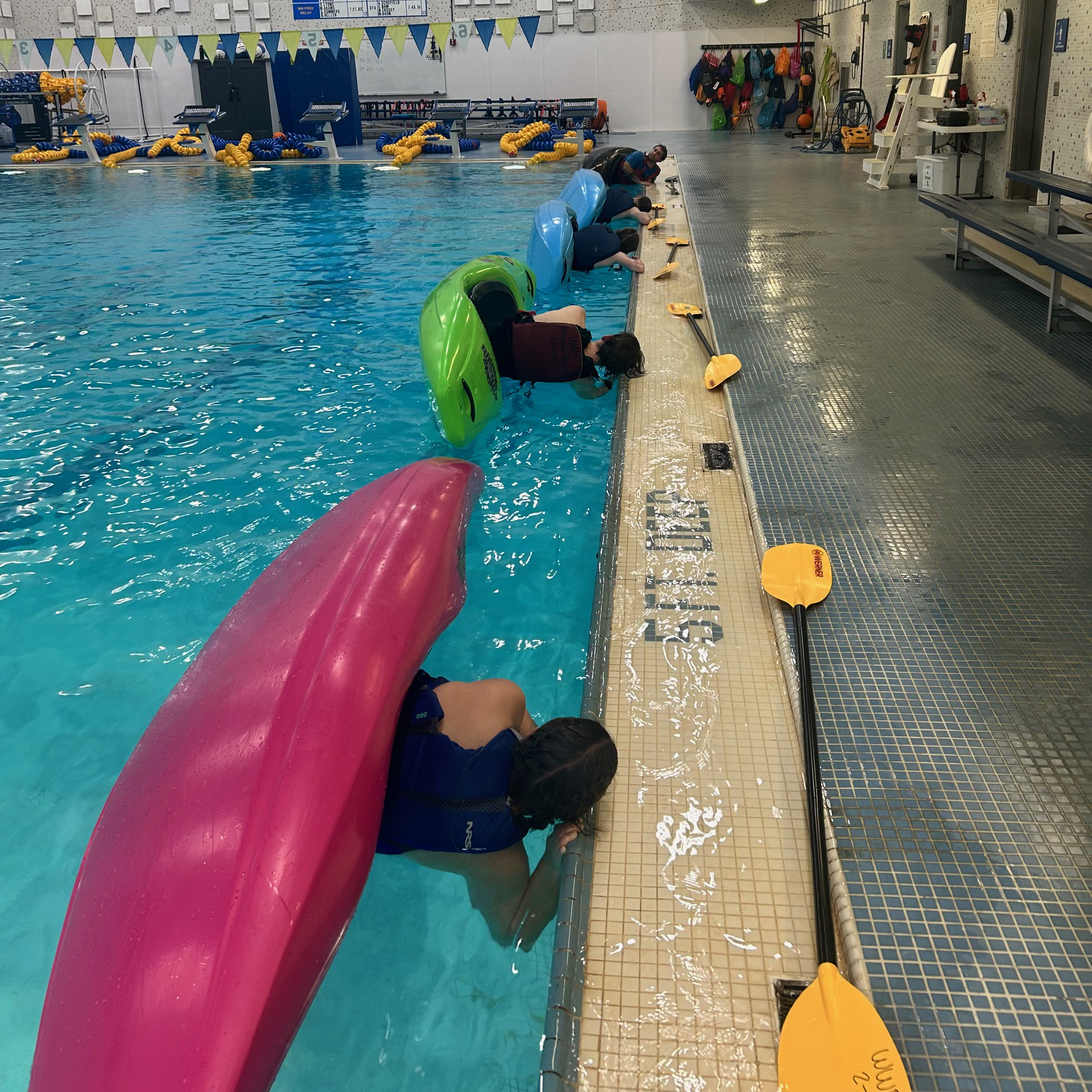 Kayakers practicing hip snaps on the pool deck.