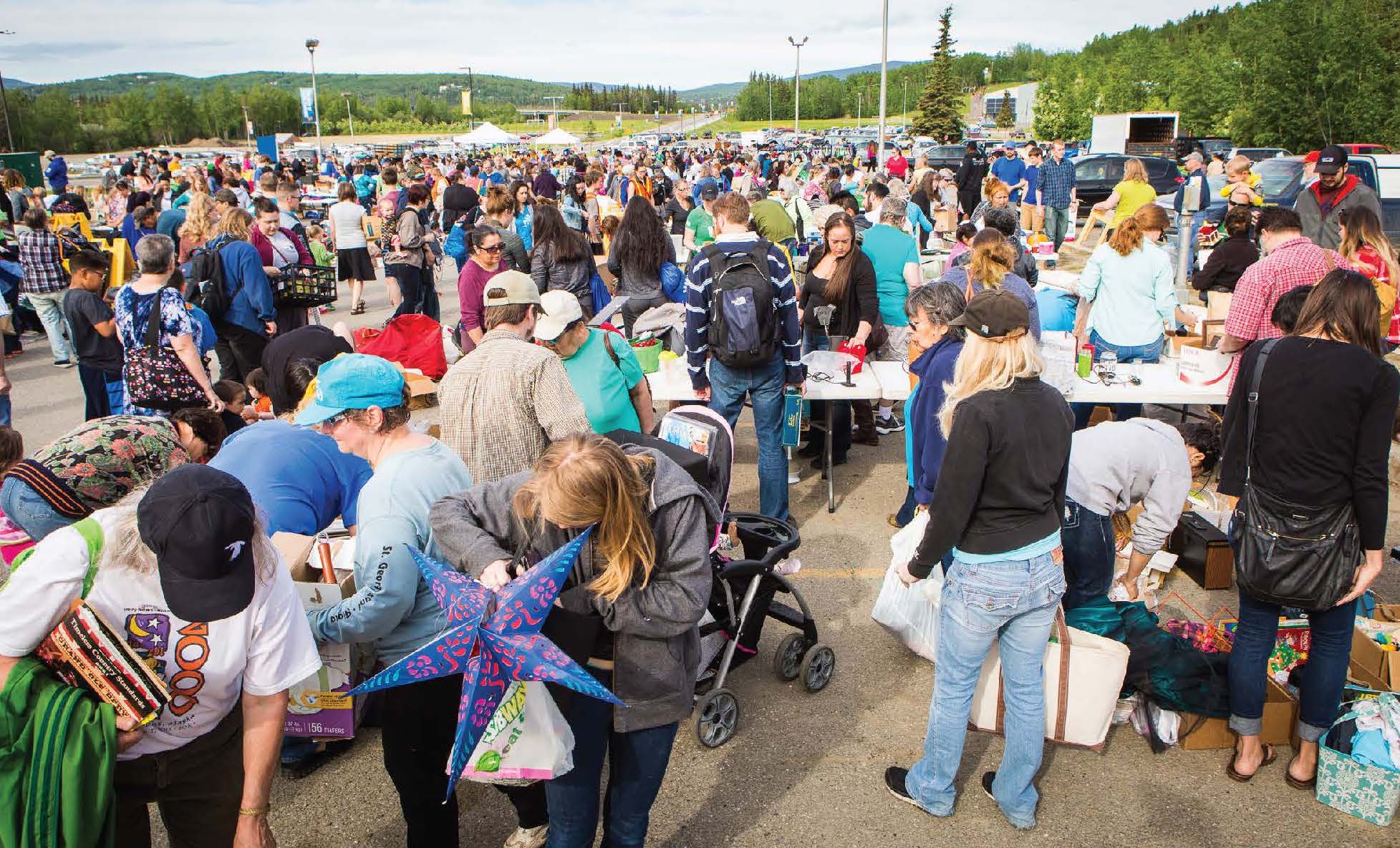 A crowd of people outdoors in a parking lot carrying and looking at miscellaneous stuff.