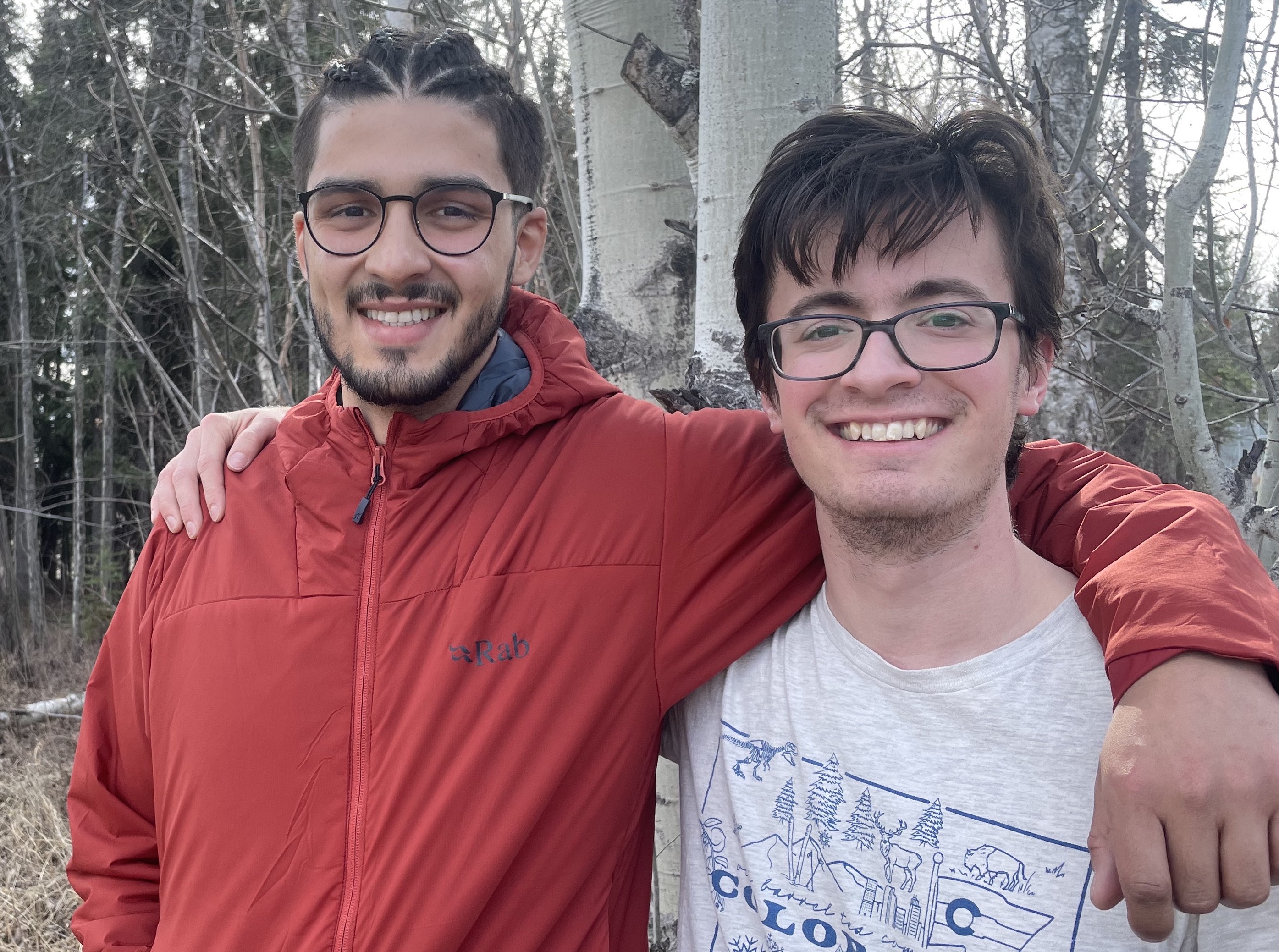close-up photo of two young men with their arms around each other's shoulders smiling at the camera