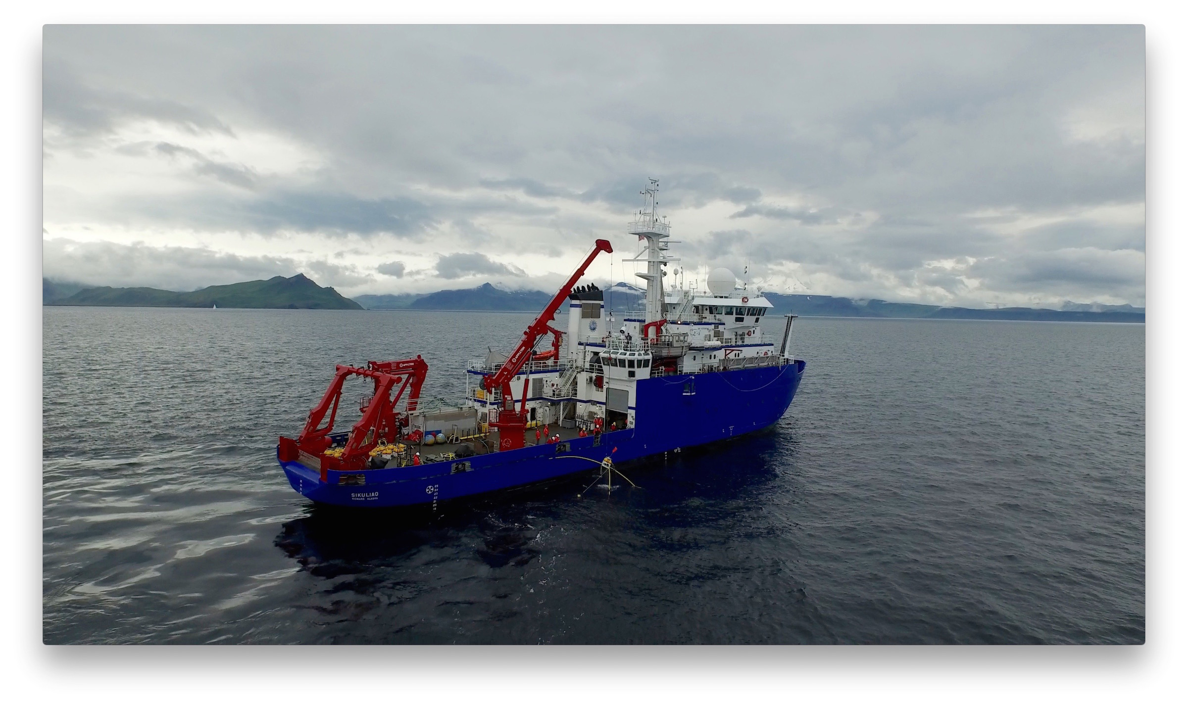 a large blue ship on the ocean with mountains in the background