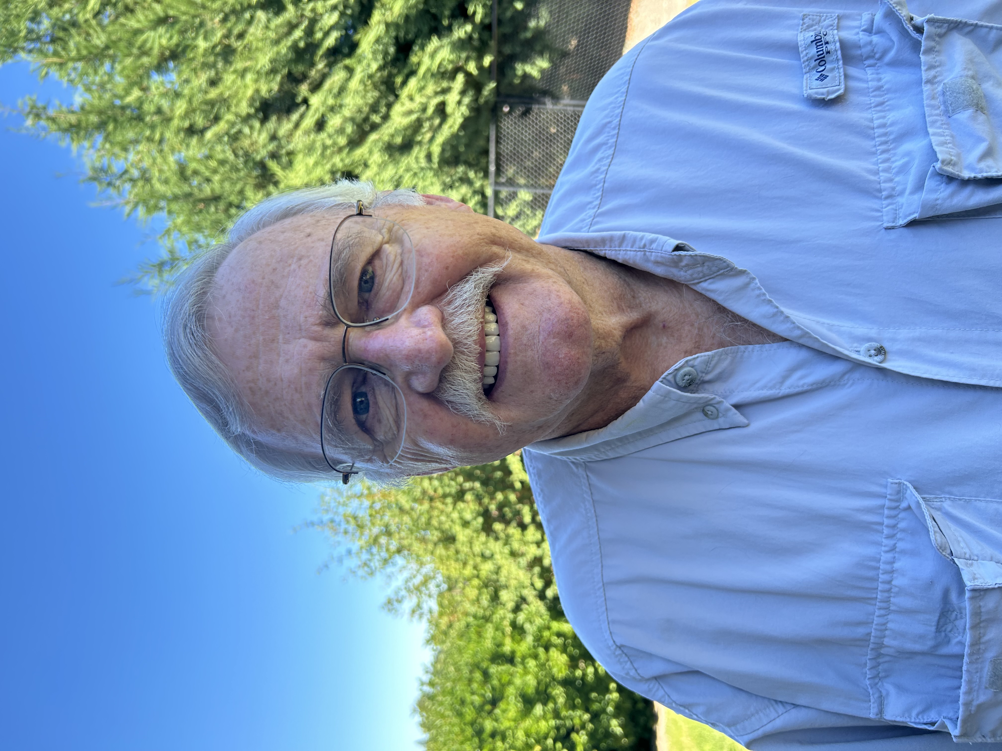 A man wearing a button-up shirt outdoors during summer.
